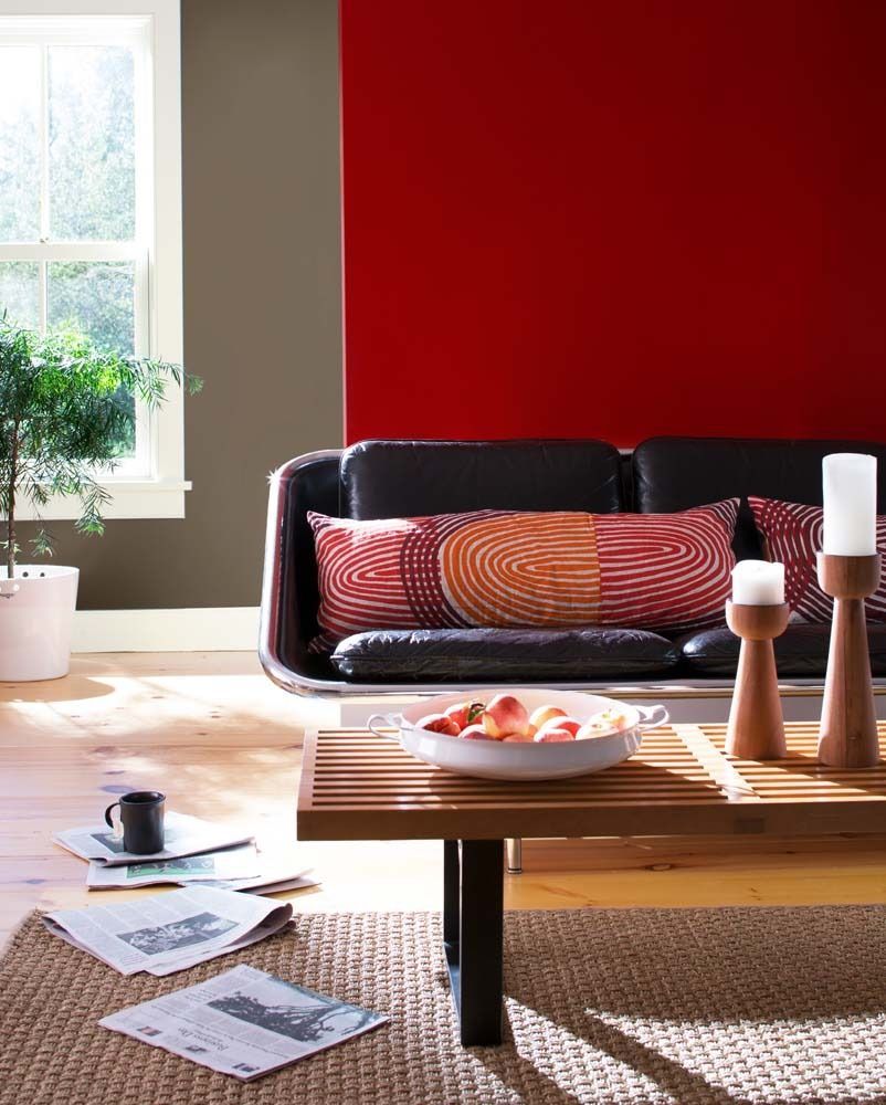 Modern living room with red accent wall, black sofa, coffee table, and sunlight by the window