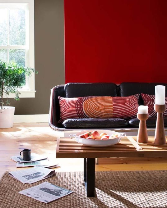Modern living room with red accent wall, black sofa, and wooden coffee table near a window