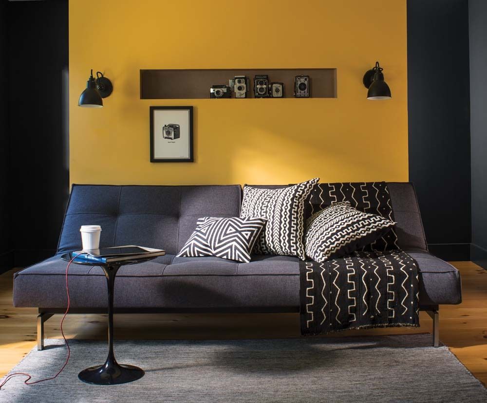 Modern living room with mustard yellow wall, navy sofa, patterned pillows, and a small round side table