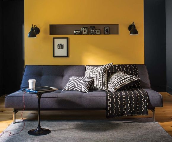 Modern living room with blue sofa, yellow accent wall, patterned pillows, and black wall sconces.