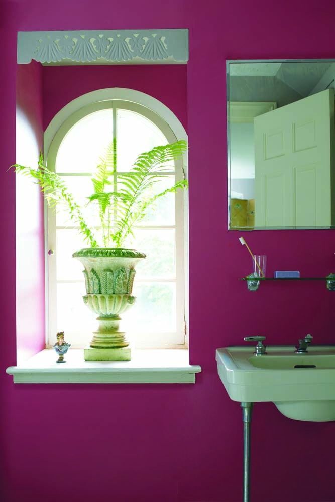 Bright magenta bathroom with a white arched window, fern, wall mirror, and sink