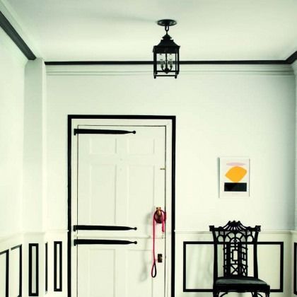 Minimalist white room with black trim, closed door, hanging lantern light, and small wall art above a black chair.