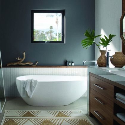 Modern bathroom with a freestanding white tub, dark wood vanity, plants, and a window view