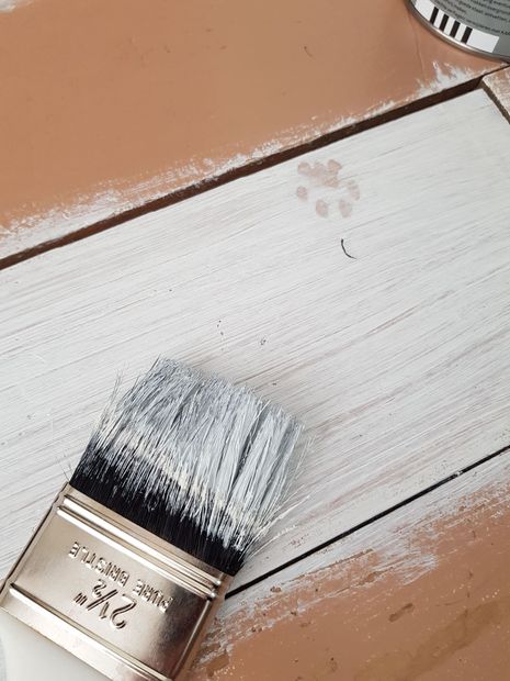 Paintbrush spreading white paint on a brown wooden surface