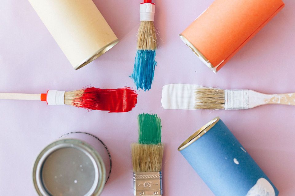 Paint brushes arranged in a circle with colorful paint tips on a pastel pink background