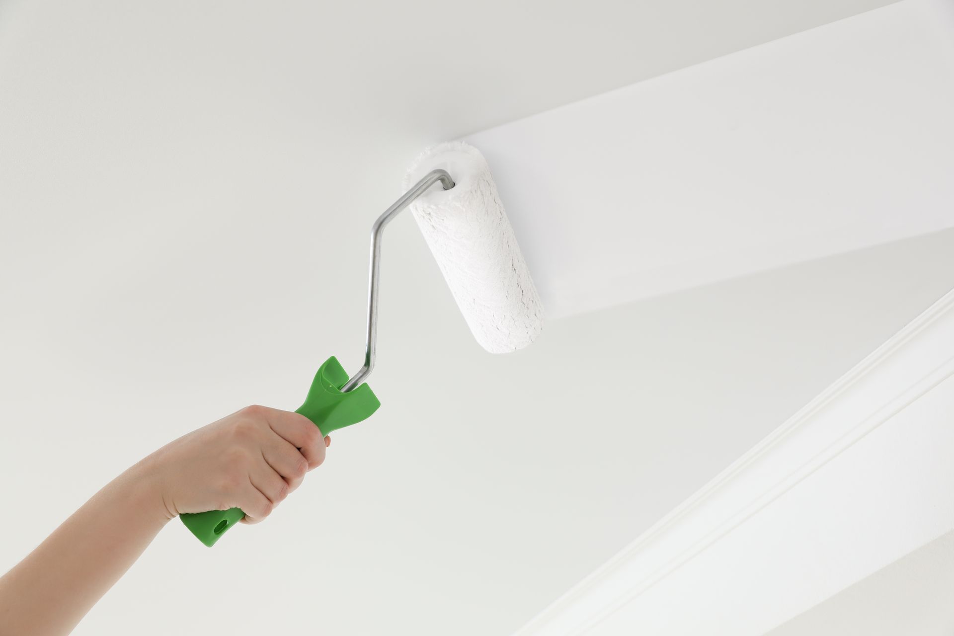 Hand painting a white wall with a green-handled roller