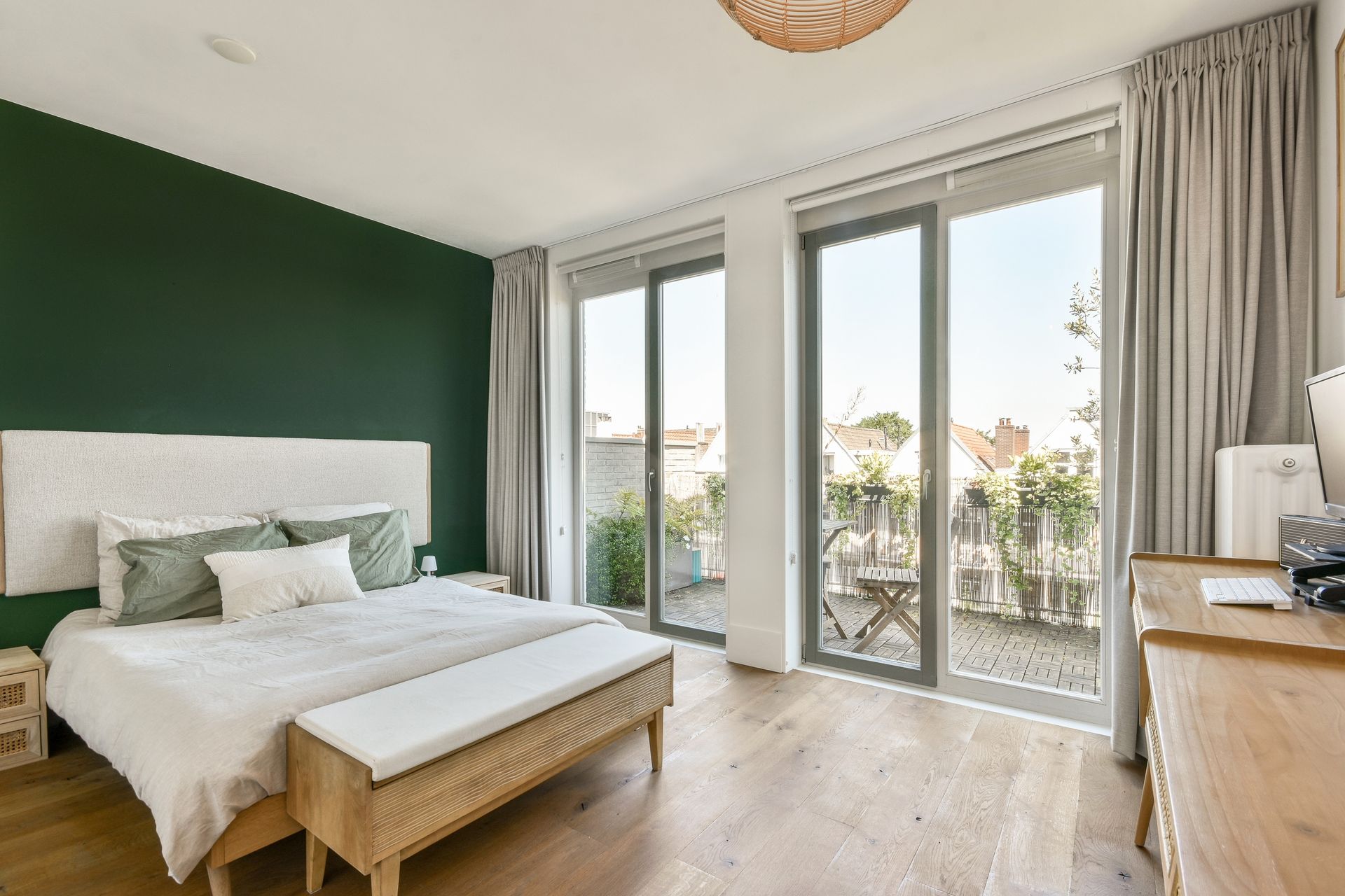 Bright bedroom with green accent wall, large windows, and a wooden bed with white bedding.