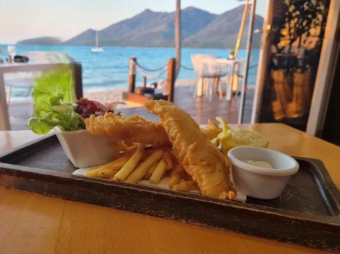 Fish and chips on a wooden tray, seaside restaurant view — The Beach Bar and Restaurant at Montes in Cape Gloucester, QLD