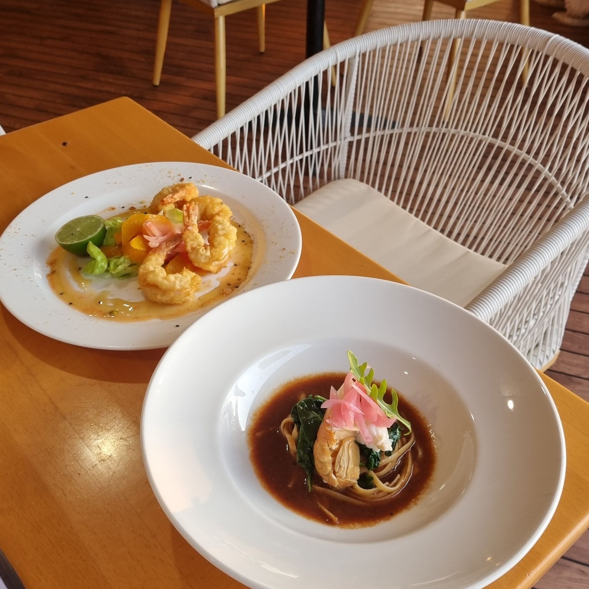 Two plates of food on a table near a white woven chair — The Beach Bar and Restaurant at Montes in Cape Gloucester, QLD