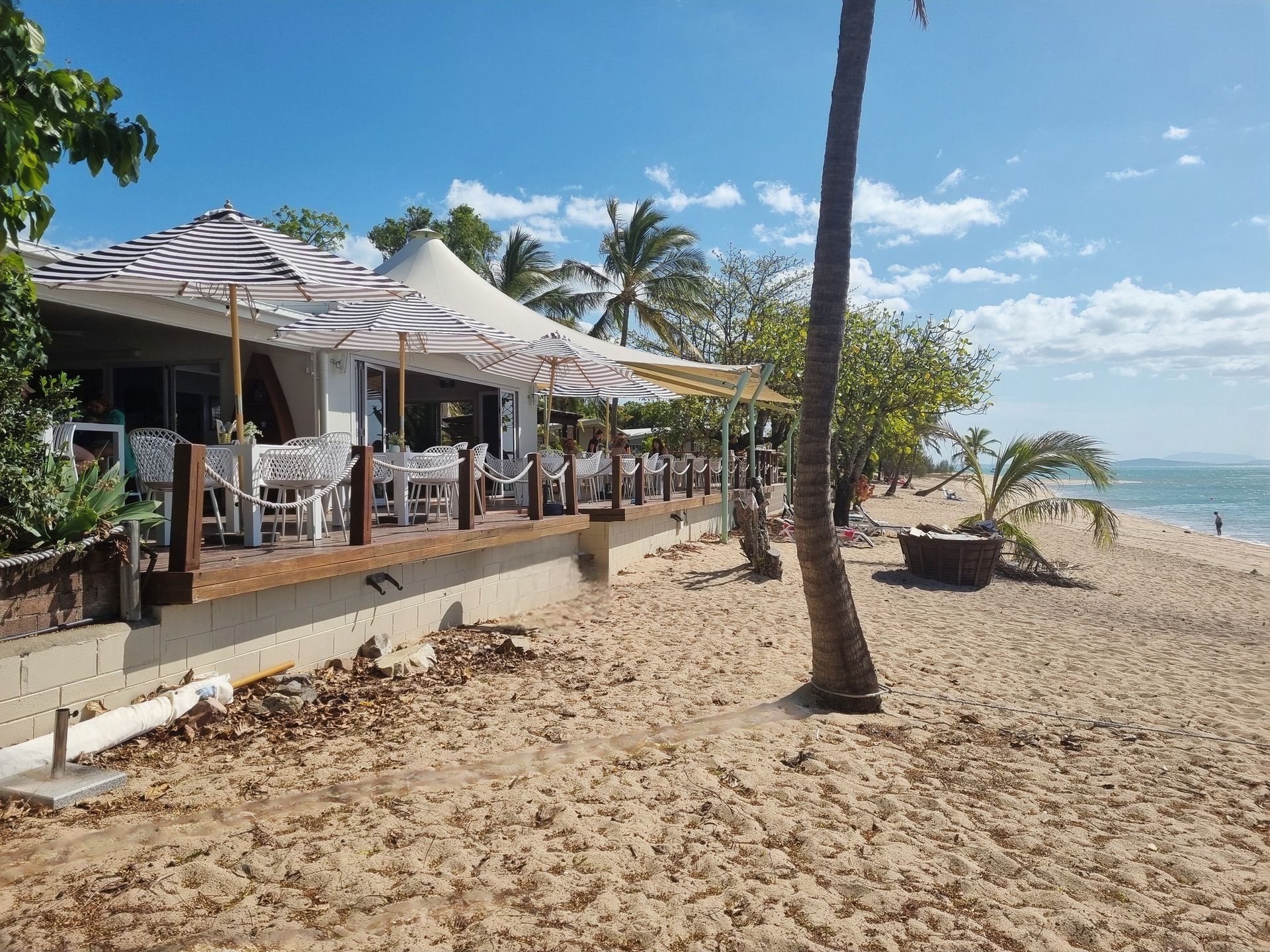 Restaurant with striped umbrellas and tables on a beach — The Beach Bar and Restaurant at Montes in Cape Gloucester, QLD