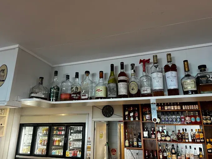 Bar with liquor bottles on shelves, above a cooler — The Beach Bar and Restaurant at Montes in Cape Gloucester, QLD