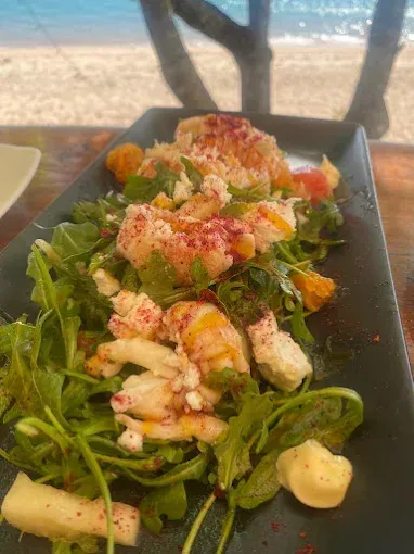 Salad with greens, seafood, and cheese, on a black plate — The Beach Bar and Restaurant at Montes in Cape Gloucester, QLD