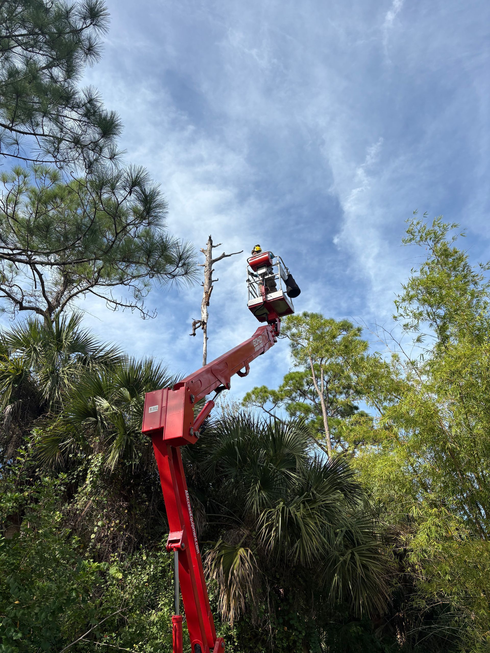 A person in a bucket lift working on a power line against a partly cloudy sky.