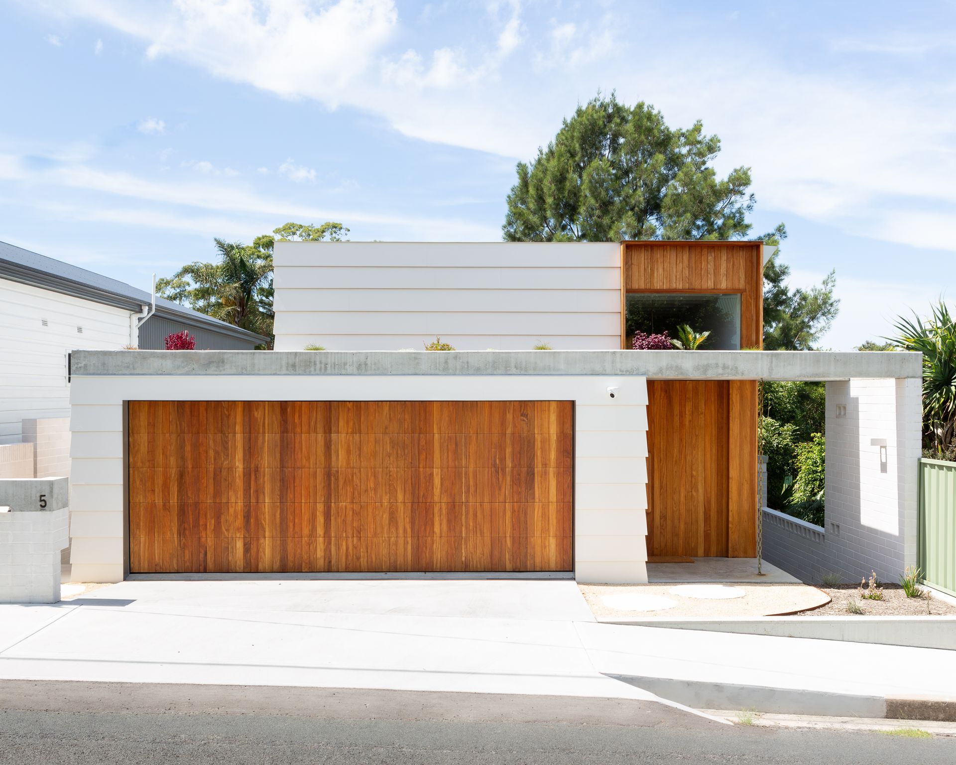 Throsby House - Modern house with wooden garage door and entrance, concrete accents, blue sky.