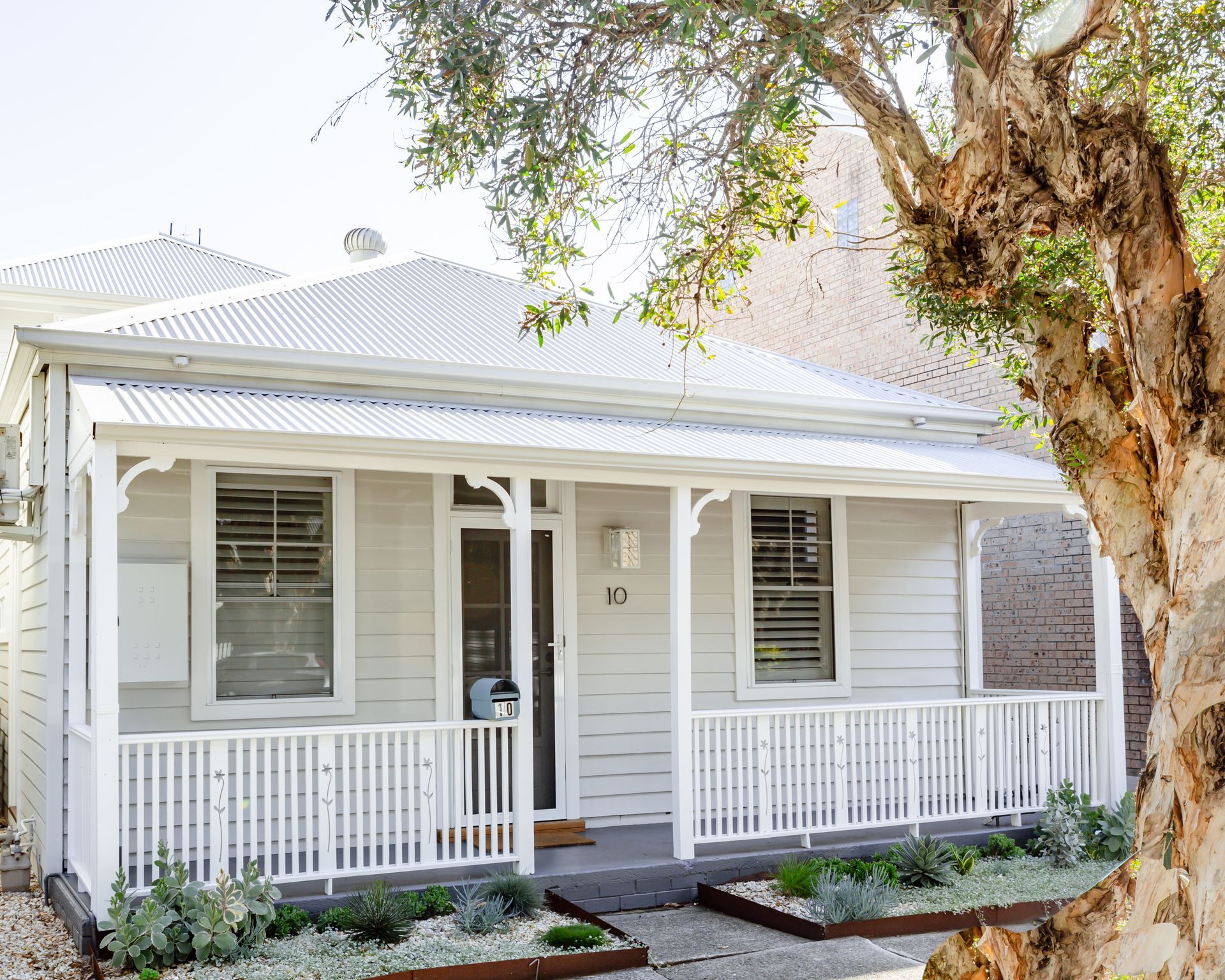 A light grey cottage with a white porch and railing, number 10 above the front door.