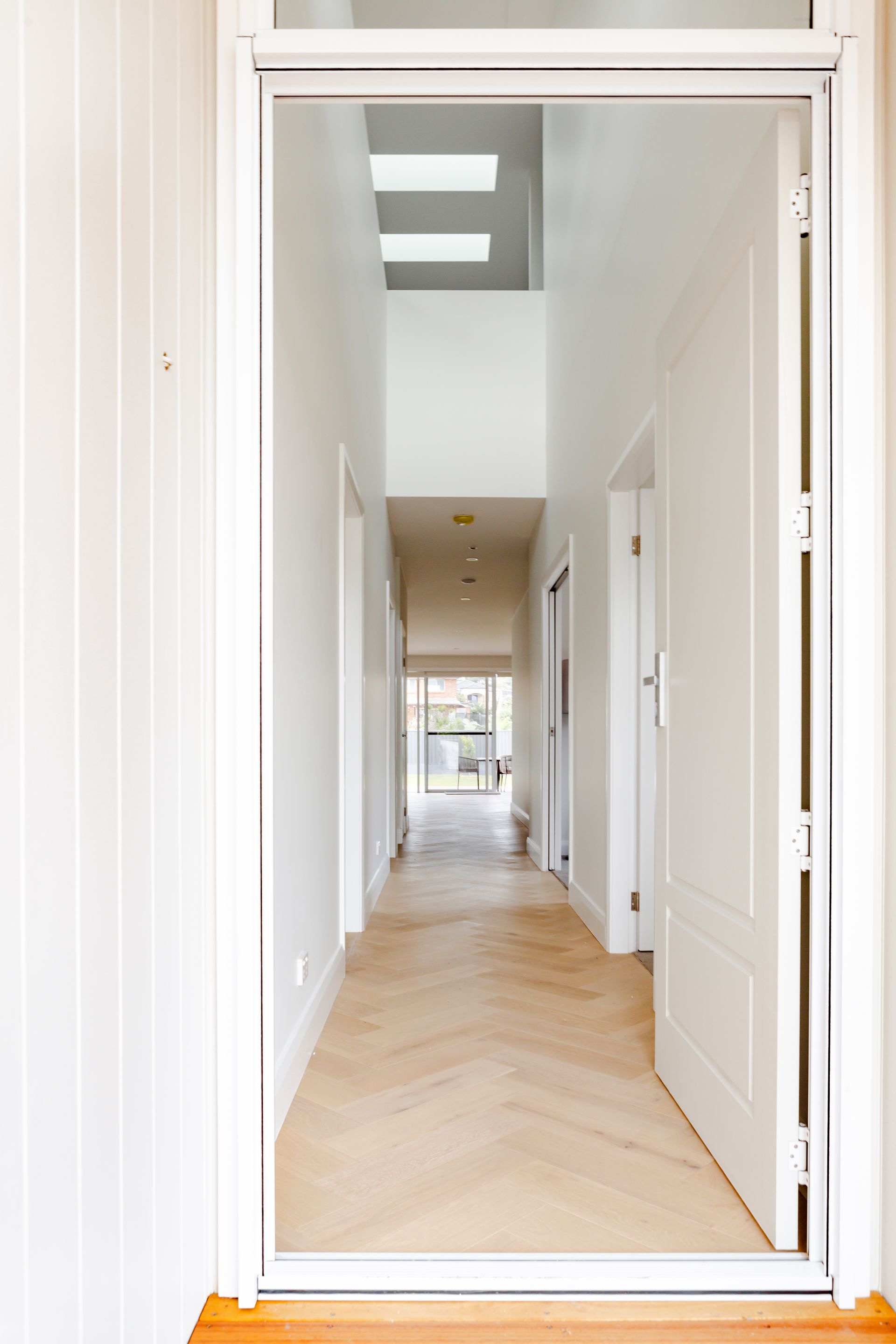 Long hallway with light wood floors, white walls, and open doors.