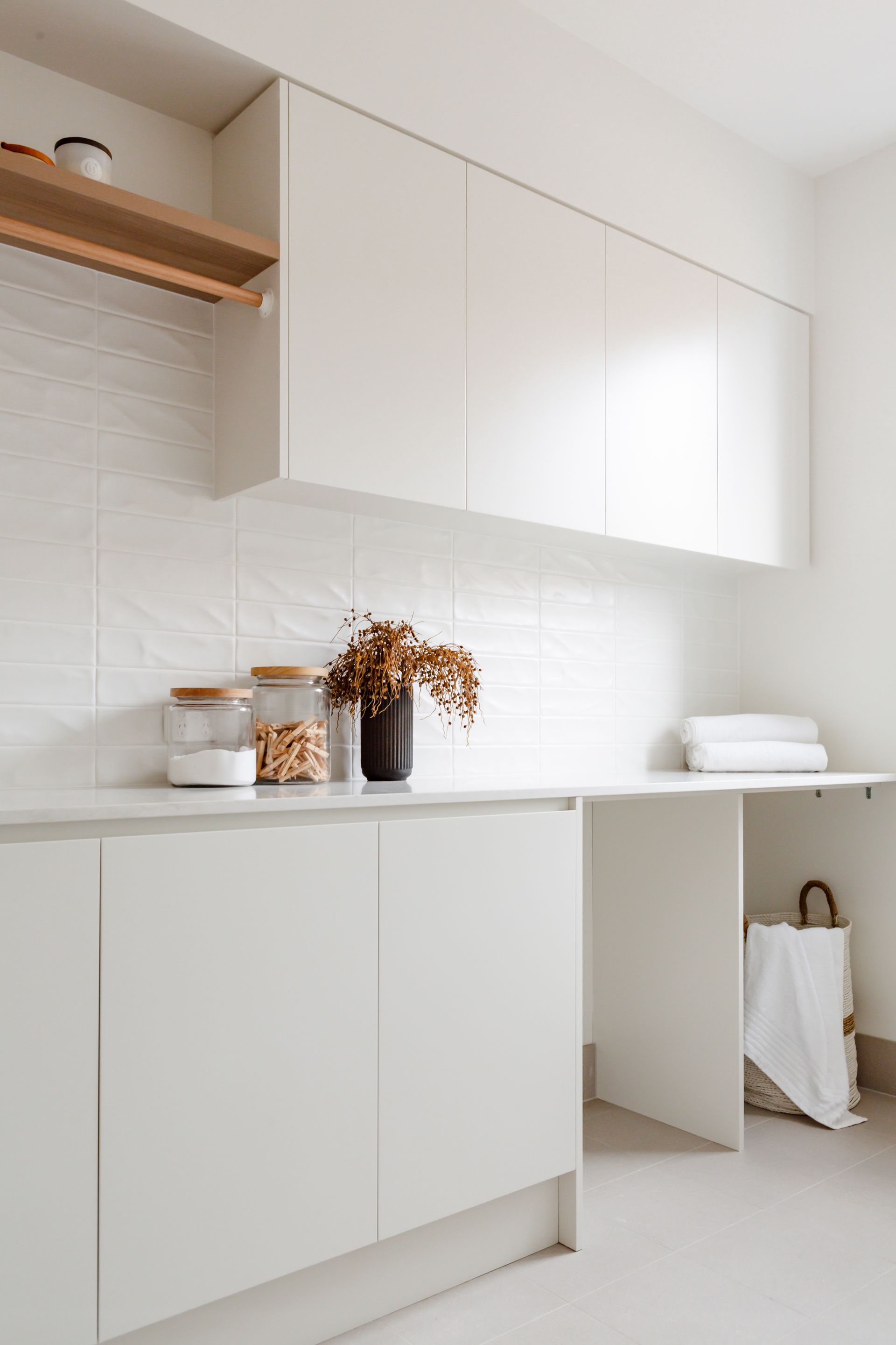 White laundry room with cabinets, counter, and shelf; jars and a vase sit on the counter.