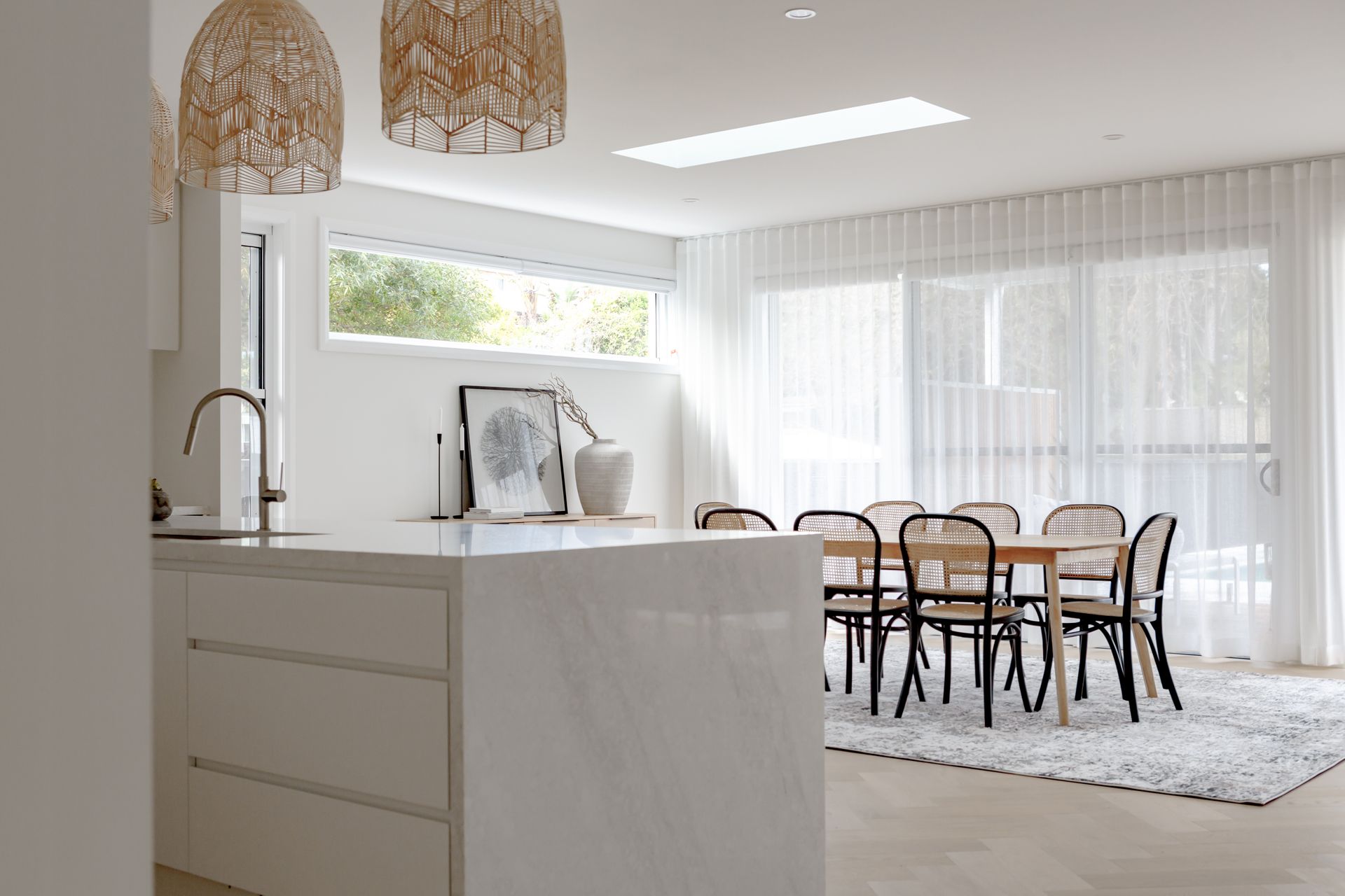 Bright white kitchen and dining area, with an island and dining table. Soft light and airy ambiance.