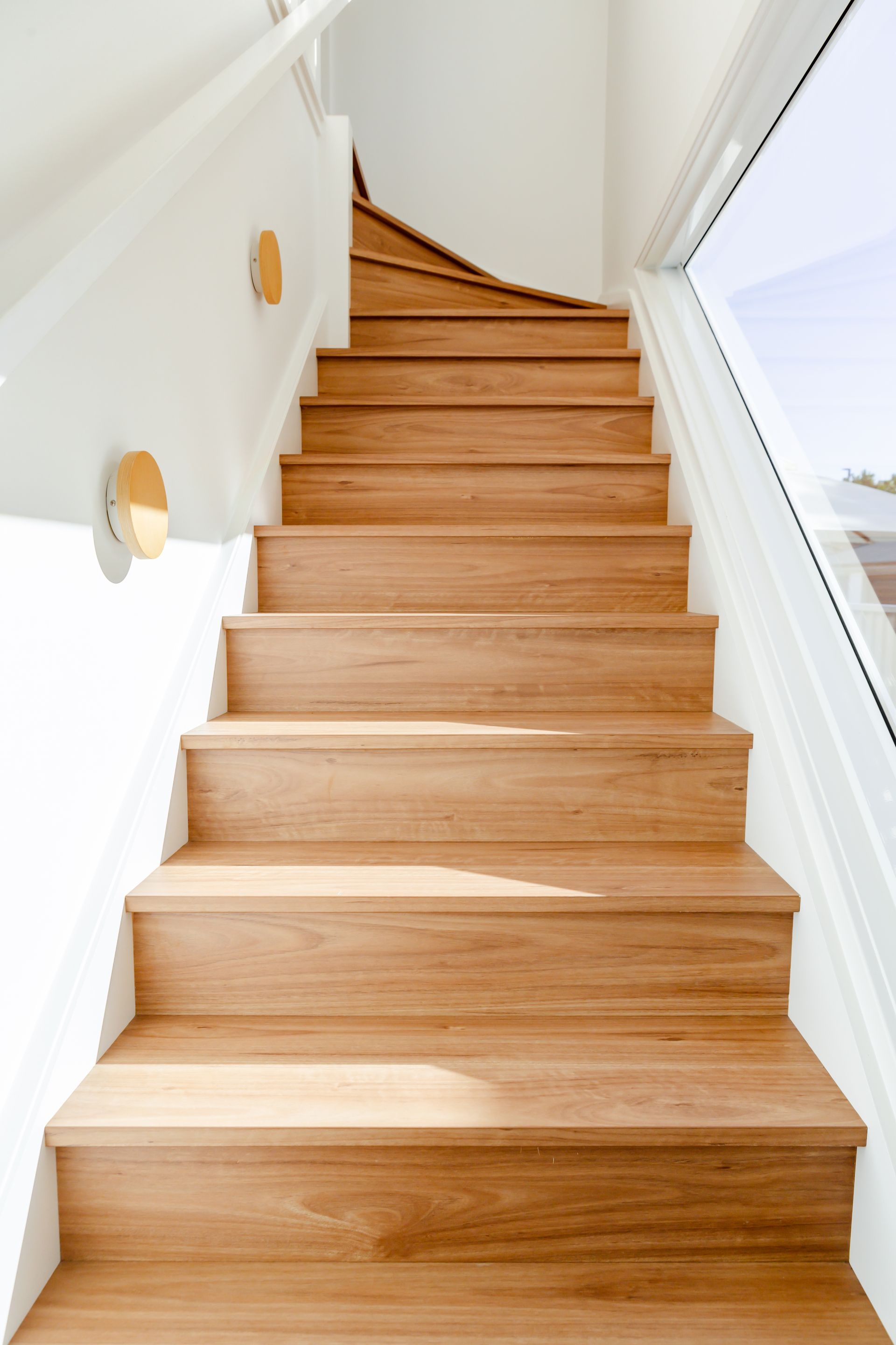 Wooden staircase leading upwards, with natural light from a window on the right.
