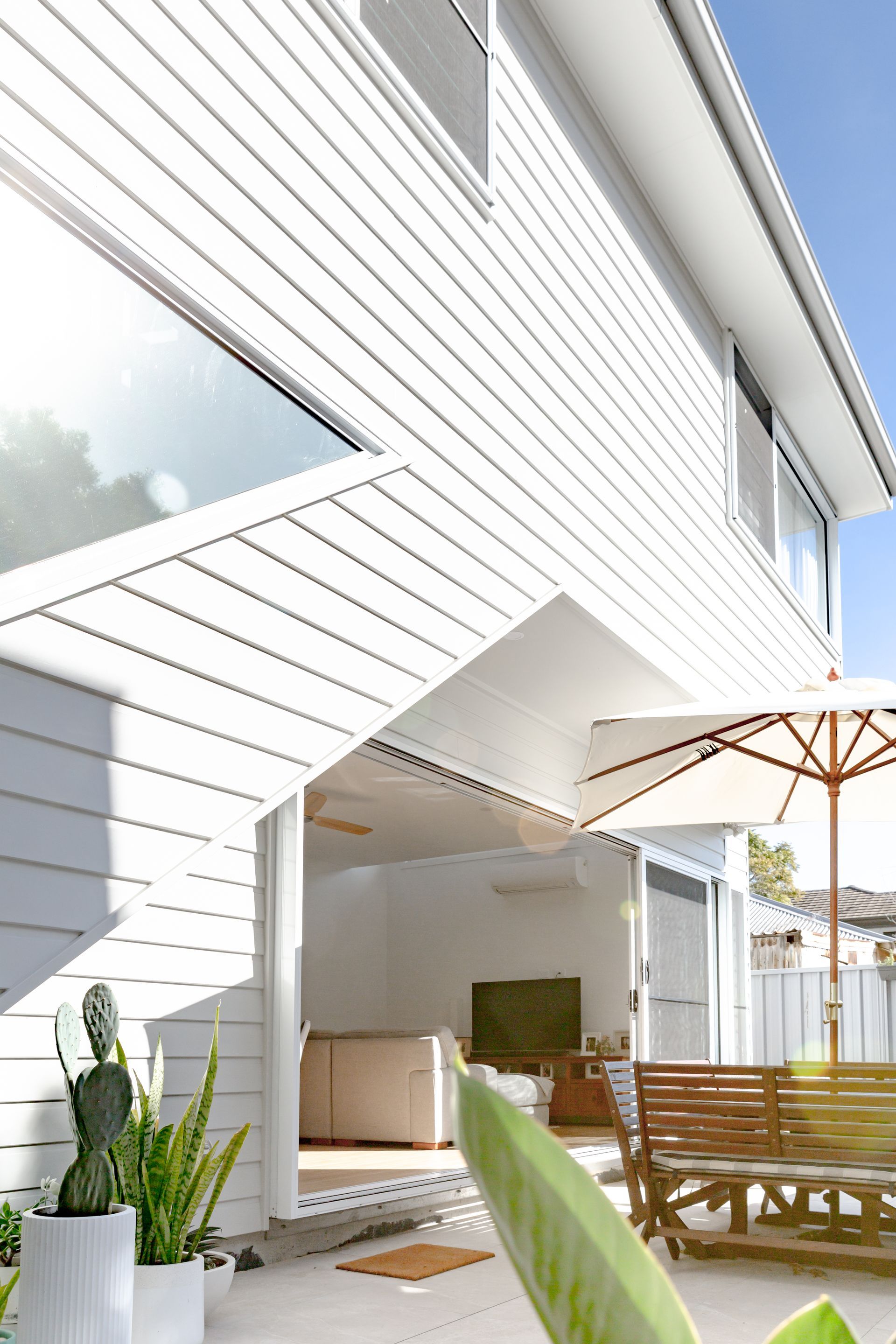 White house with outdoor patio, umbrella, and plants.