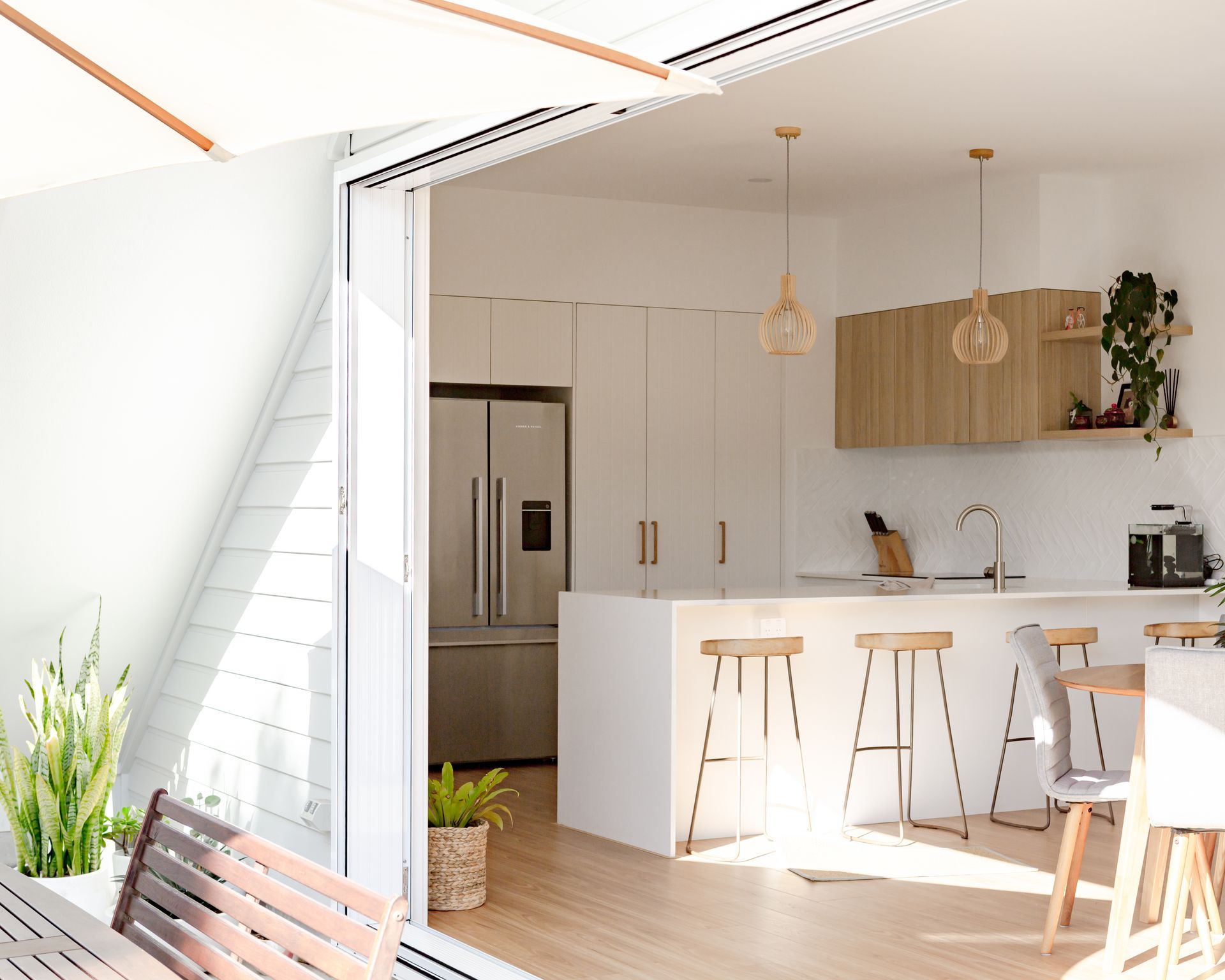 Bright, modern kitchen with white cabinets, wood accents, and open sliding doors to outdoor seating.