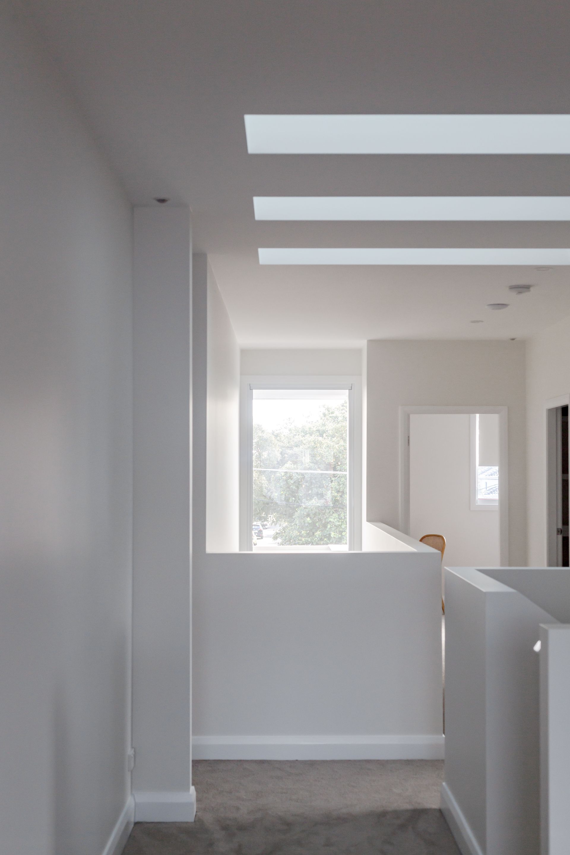 White hallway with skylights and partial walls; natural light, carpet flooring.