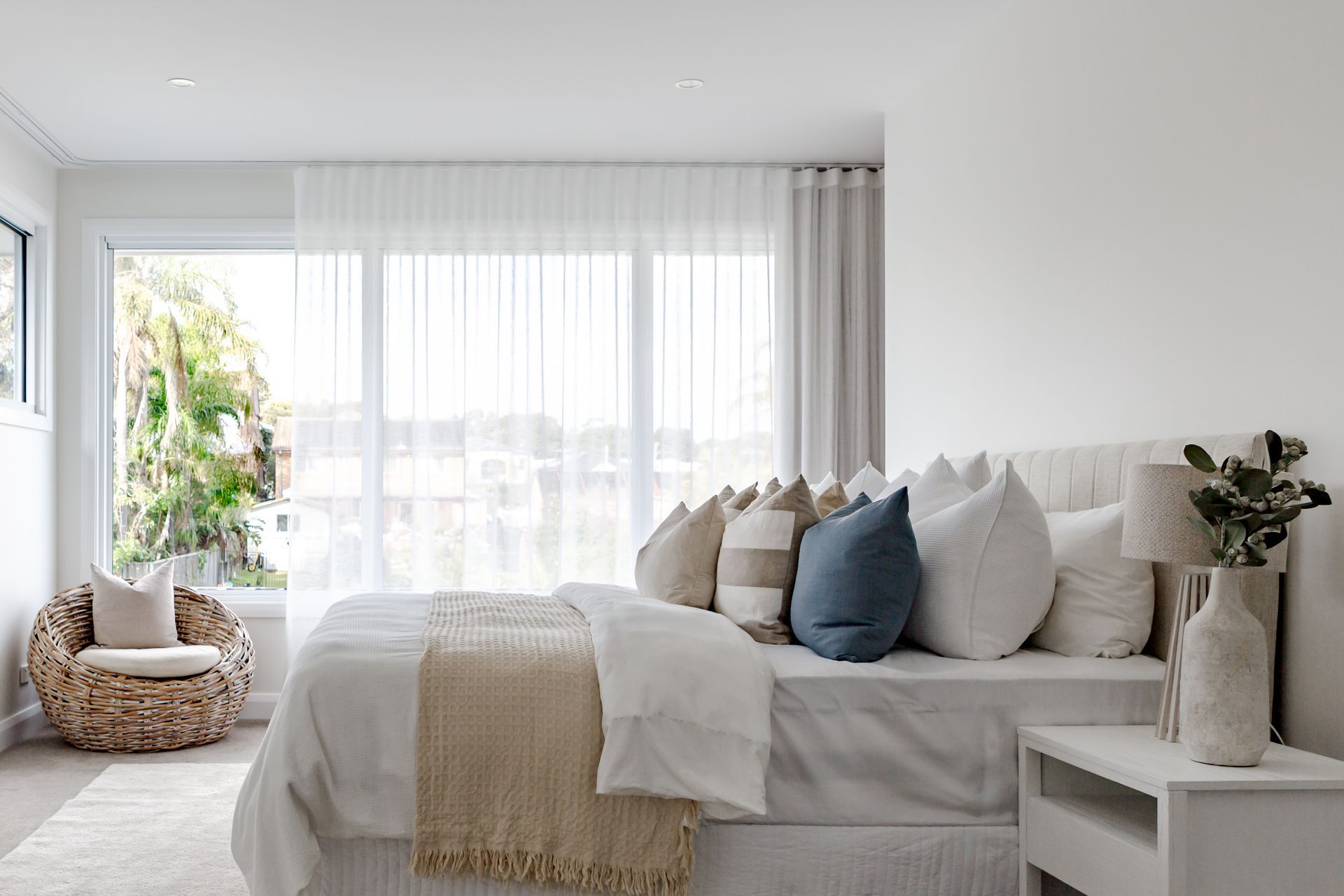 Bedroom with a bed, pillows, and a wicker chair, bathed in natural light.