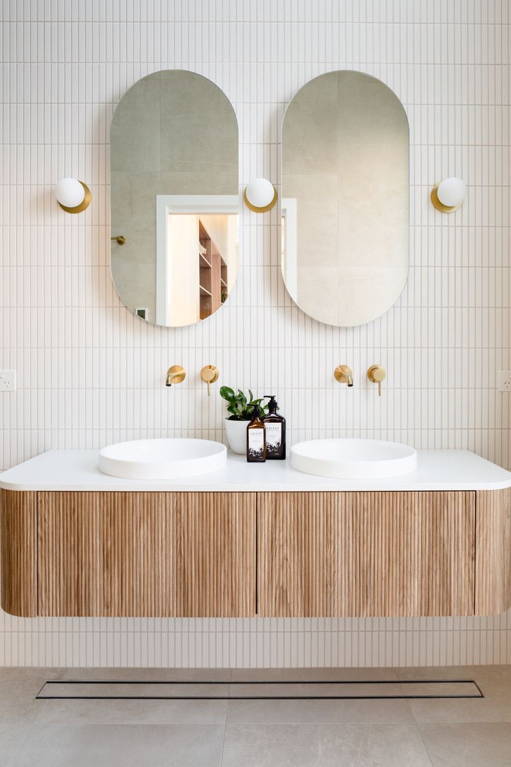 Modern bathroom with two oval mirrors, wood vanity, and white tile.