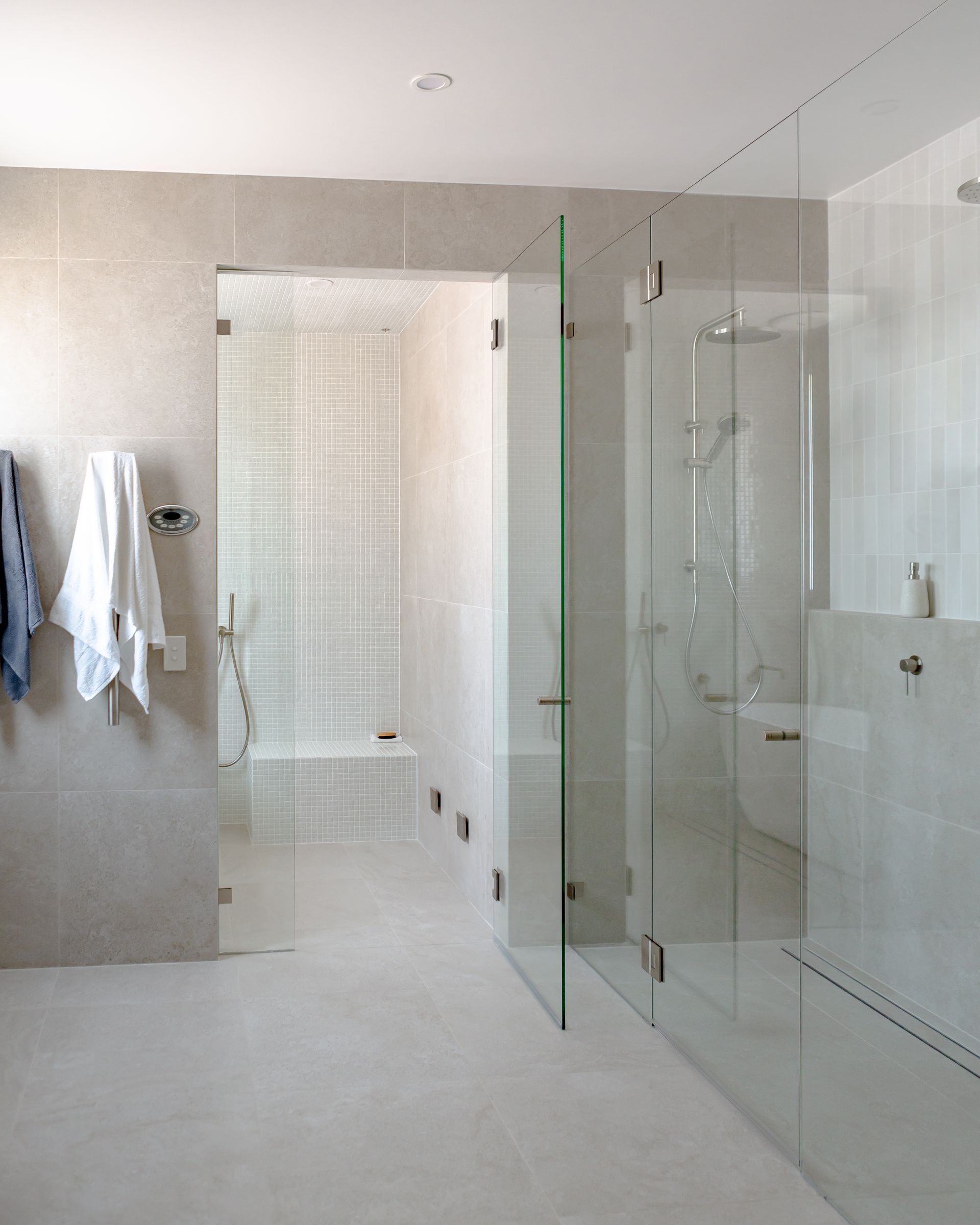 Modern bathroom with glass shower doors and tiled walls. White and gray tones throughout.