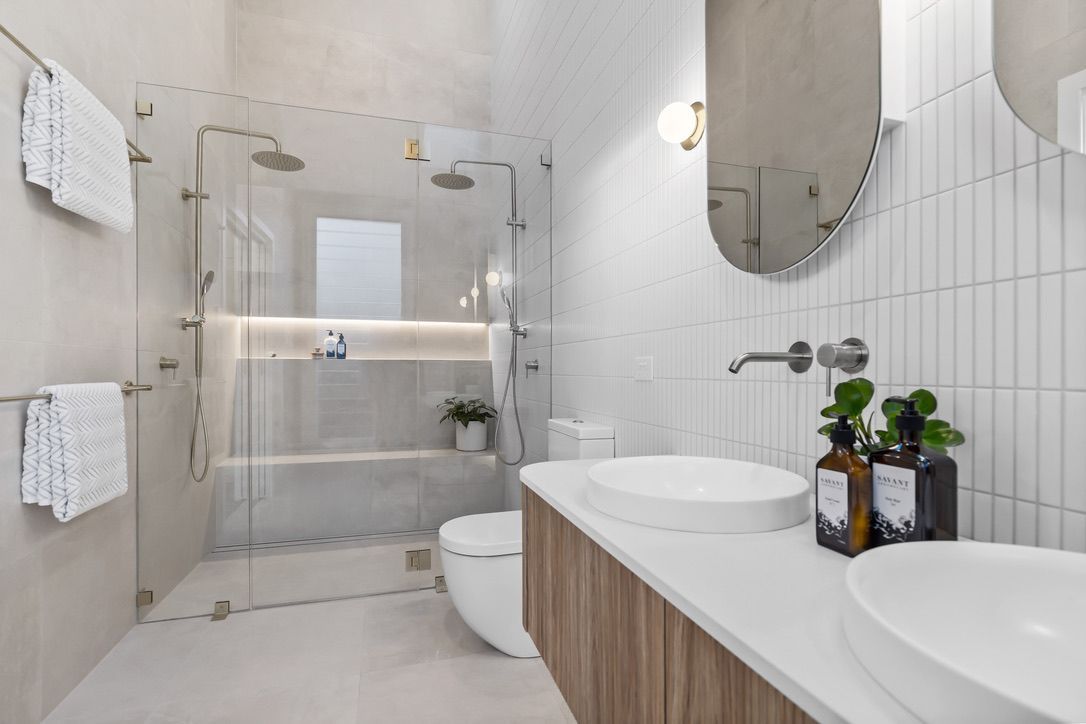Modern bathroom with glass shower, white walls, wood vanity, and double sinks.