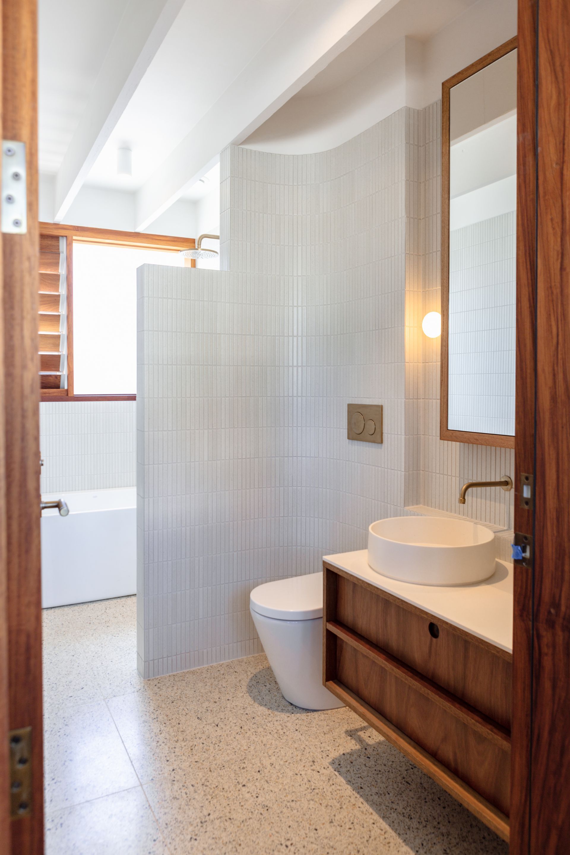Modern bathroom with white tiles, wooden vanity, and bathtub.