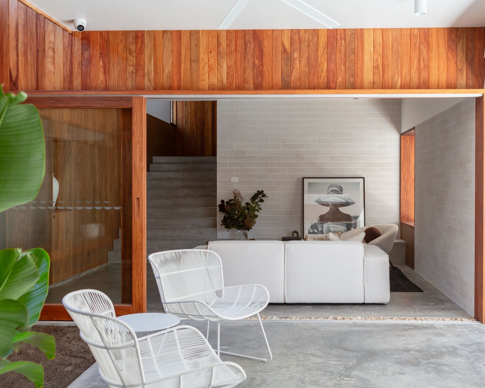 Bright, open room with white sofa, chairs, and wooden accents, concrete floors. Staircase visible.