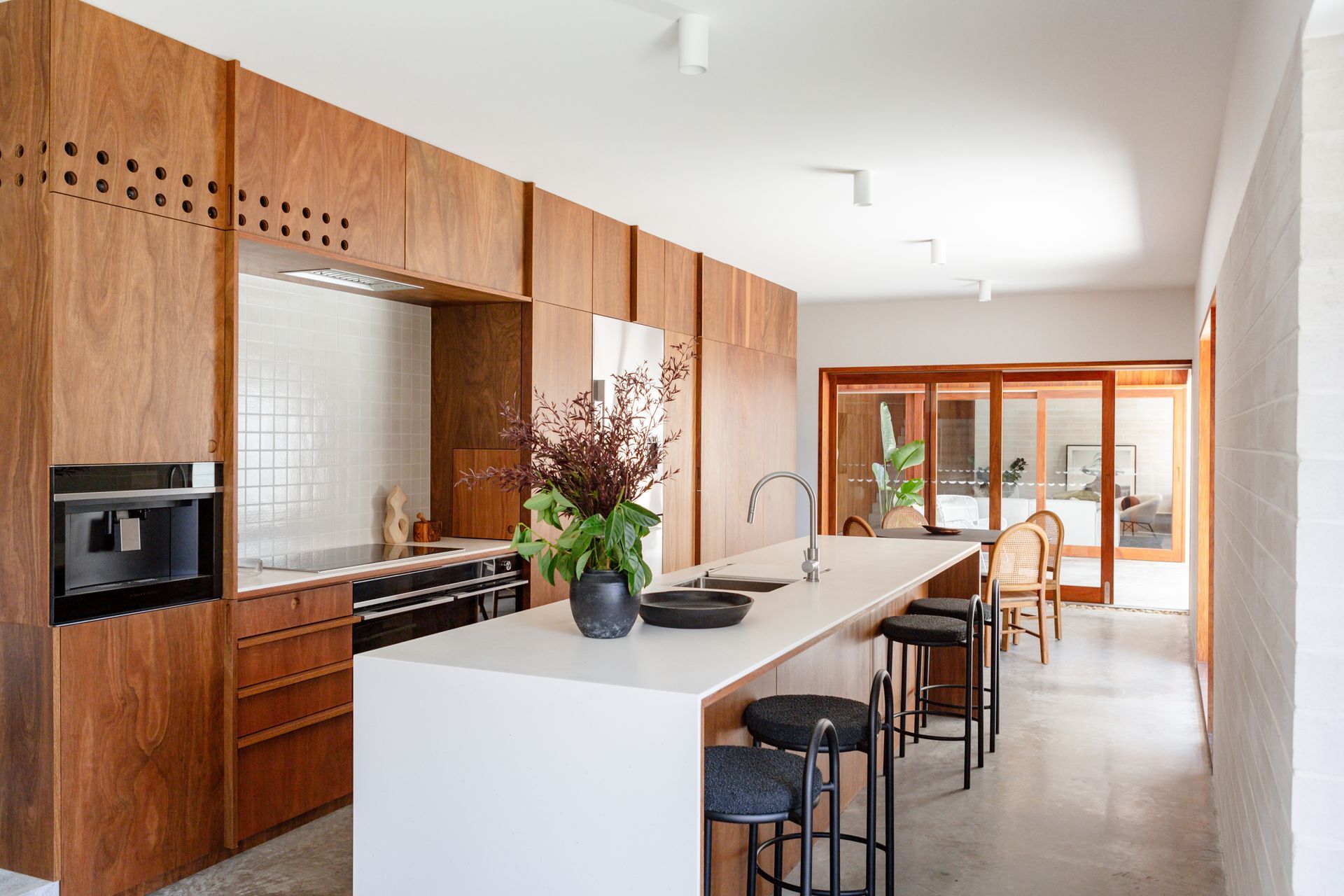 Modern kitchen with wood cabinetry, white island, and bar stools. Sliding glass doors lead to an outdoor area.