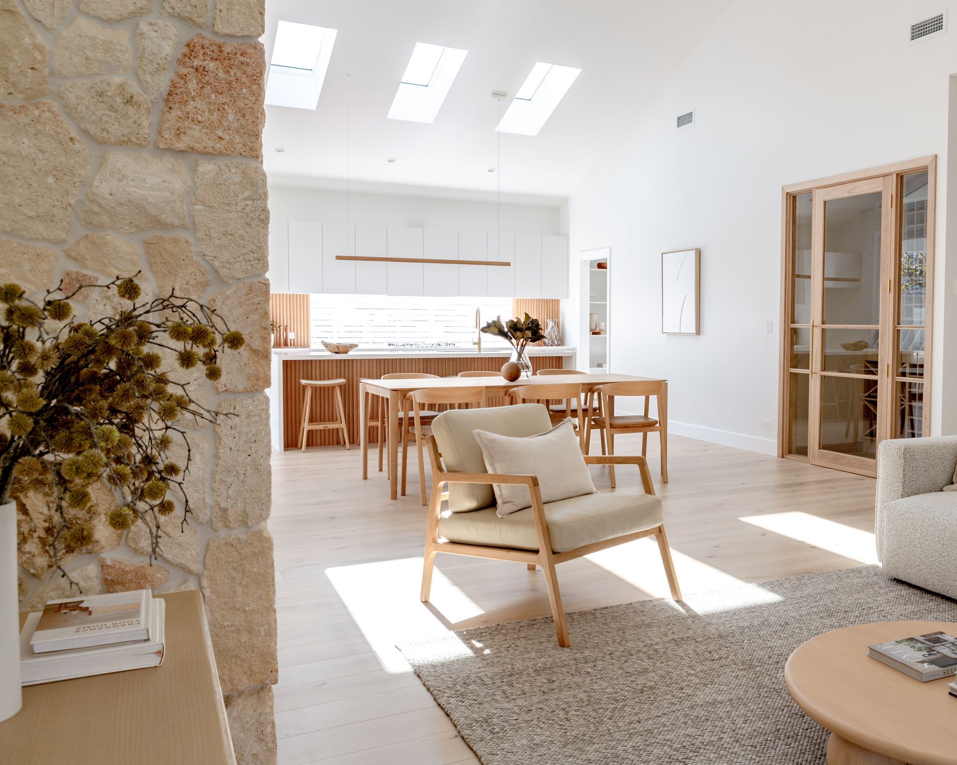 Open-concept living space with kitchen, dining, and seating areas. Neutral tones, natural light, and stone accent wall.
