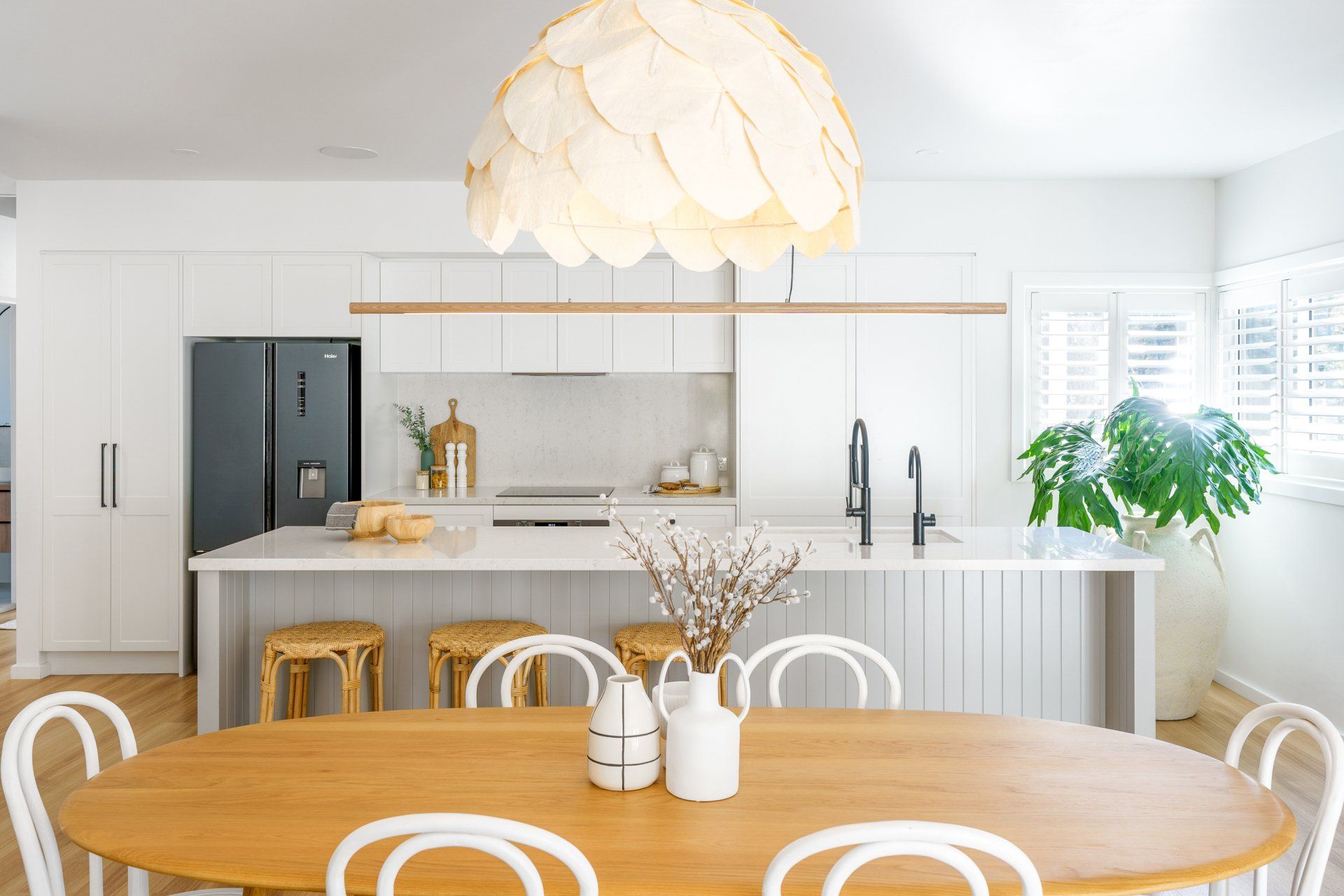 Kitchen with wooden table, white chairs, island, and light fixture; a fridge is on the left.