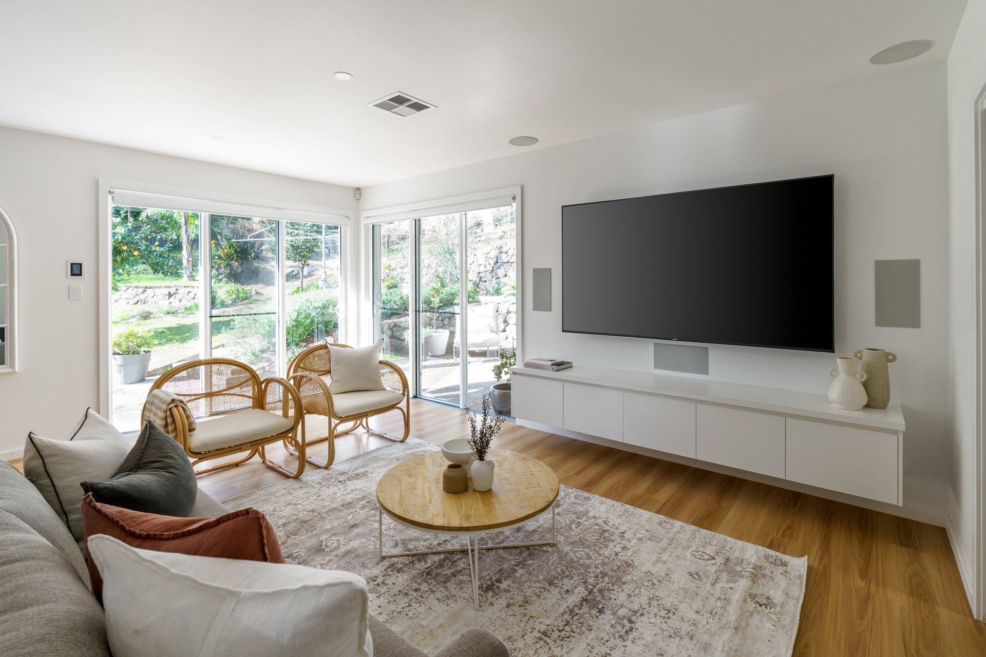 Living room with large TV, white cabinets, wood floor, and wicker chairs.