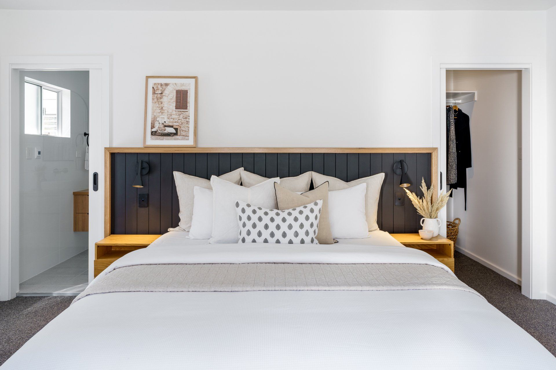 Bedroom with king-size bed, neutral tones, built-in headboard with sconces, framed art, and access to a bathroom and closet.