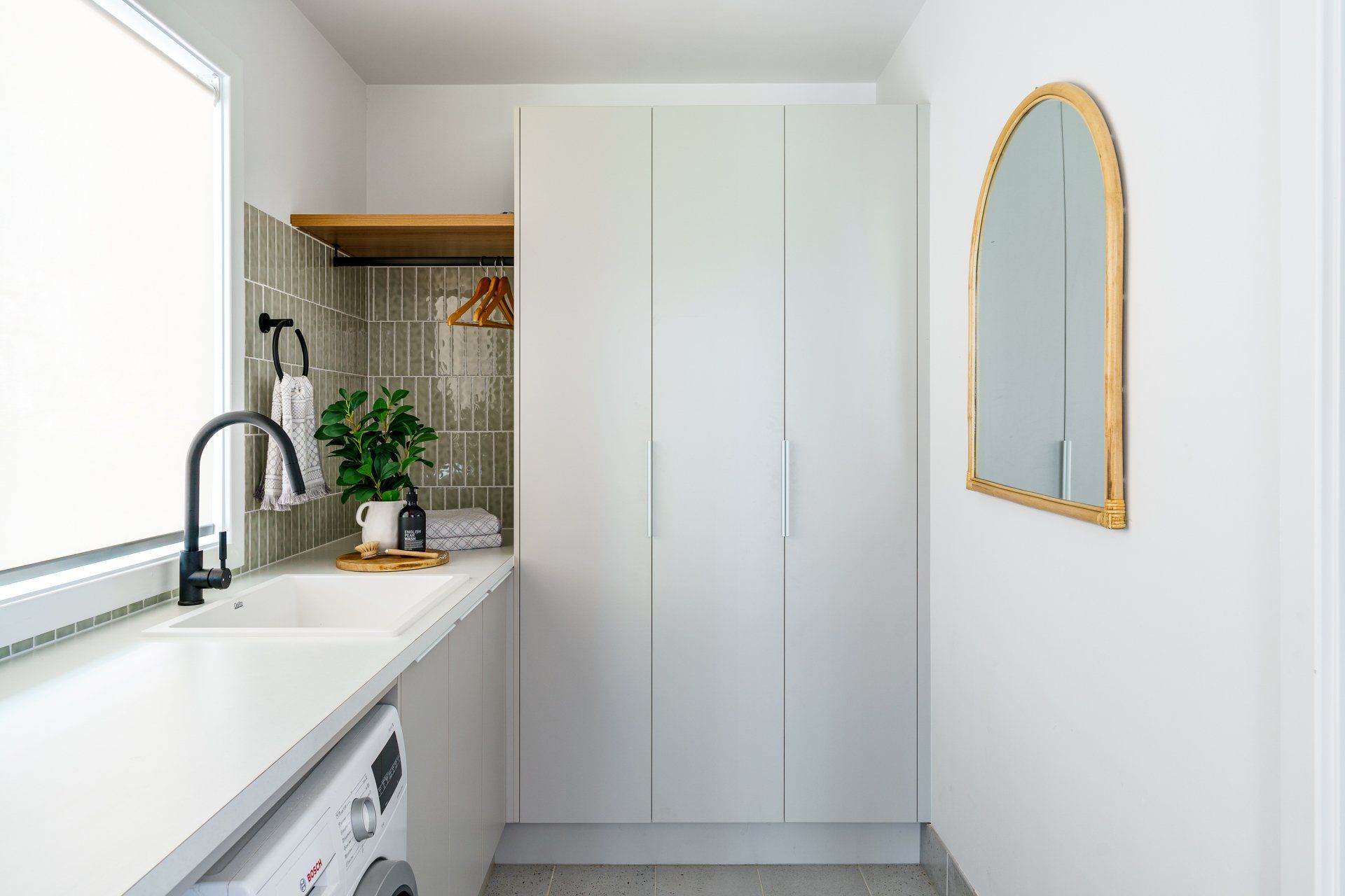 Laundry room with white cabinets, sink, gold-framed mirror, and washing machine.