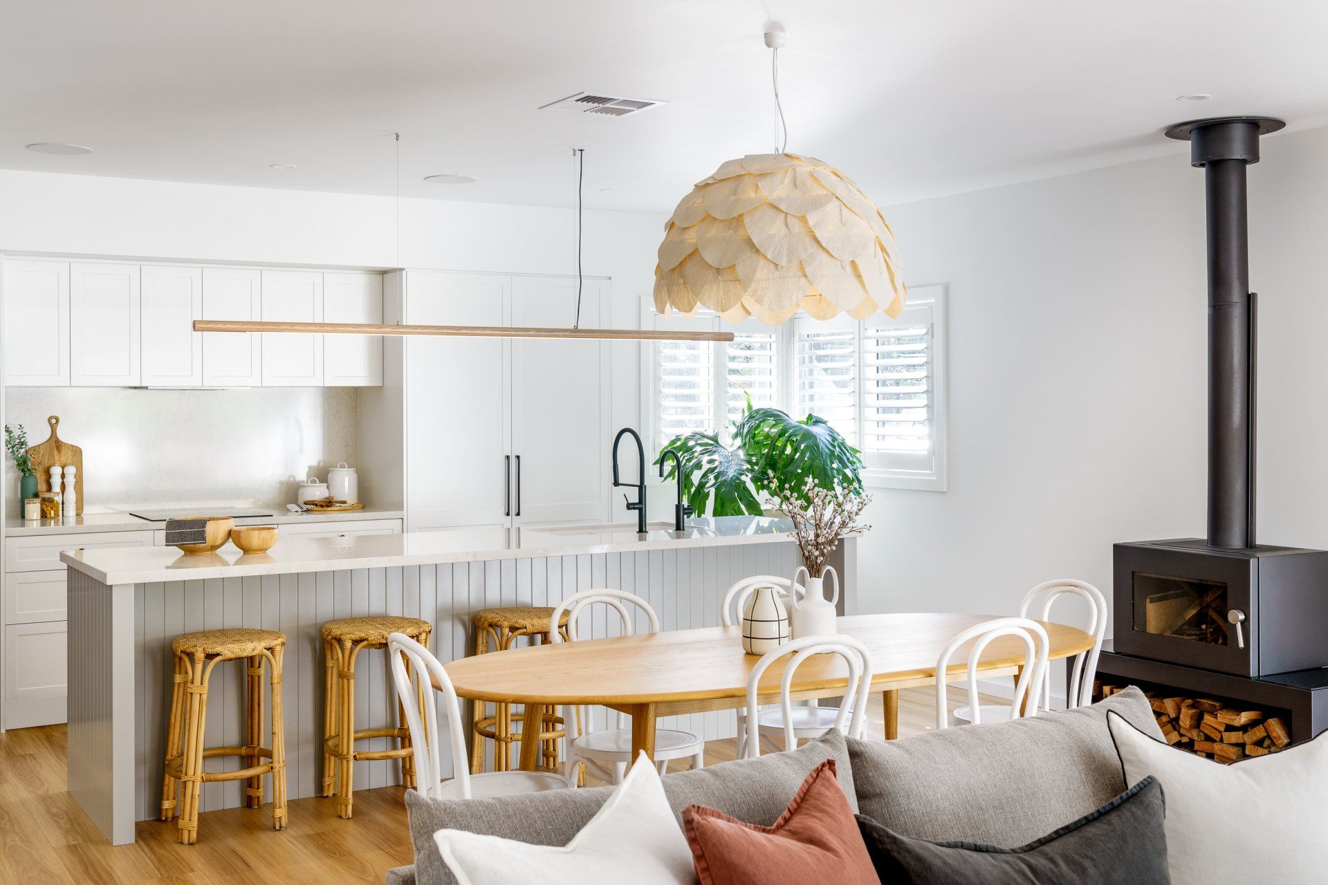 Open-concept kitchen and dining area with island, table, wood stove, and hanging light fixtures.