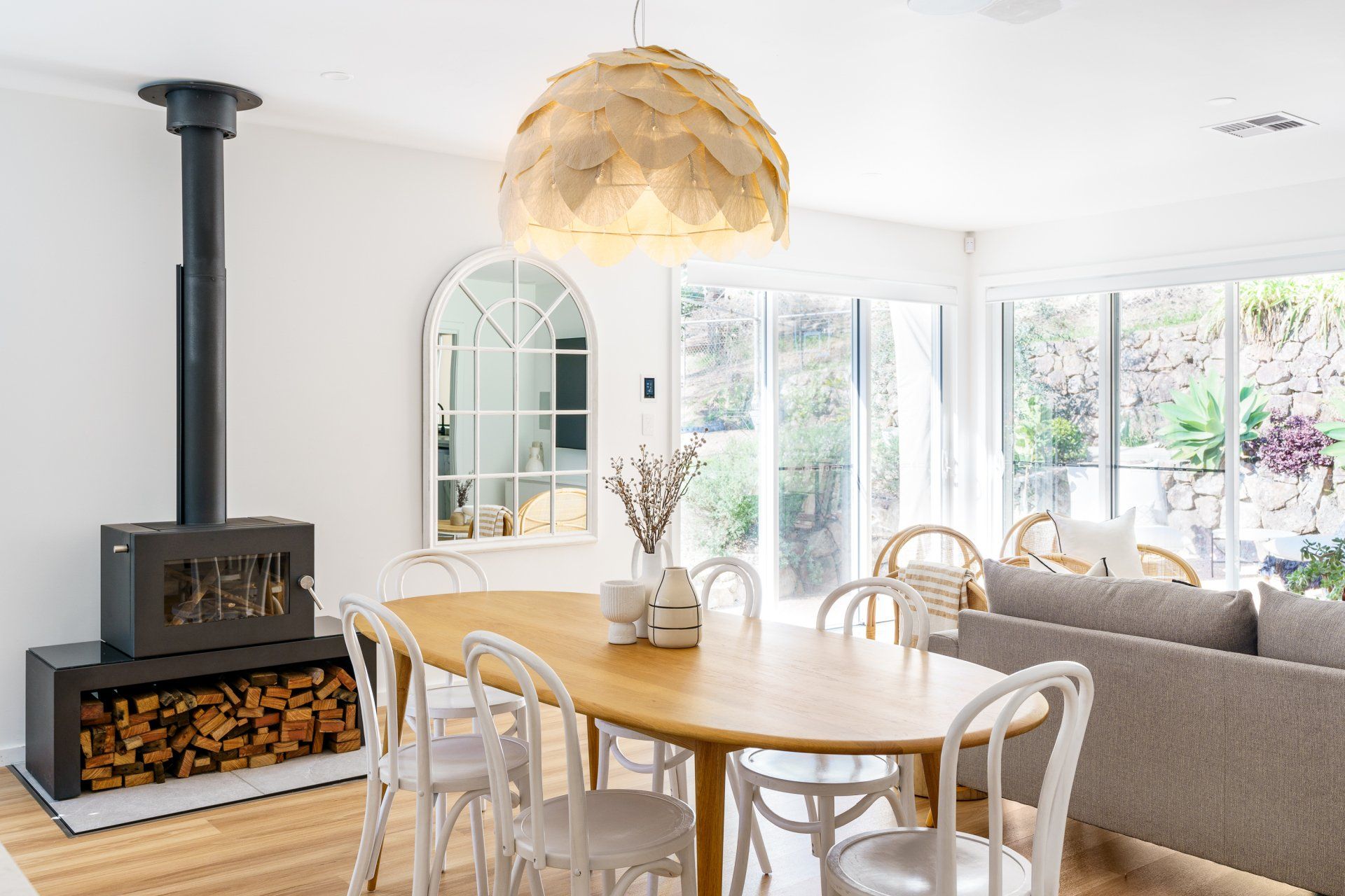 Dining room with wood-burning stove, oval table, white chairs, and large pendant light.