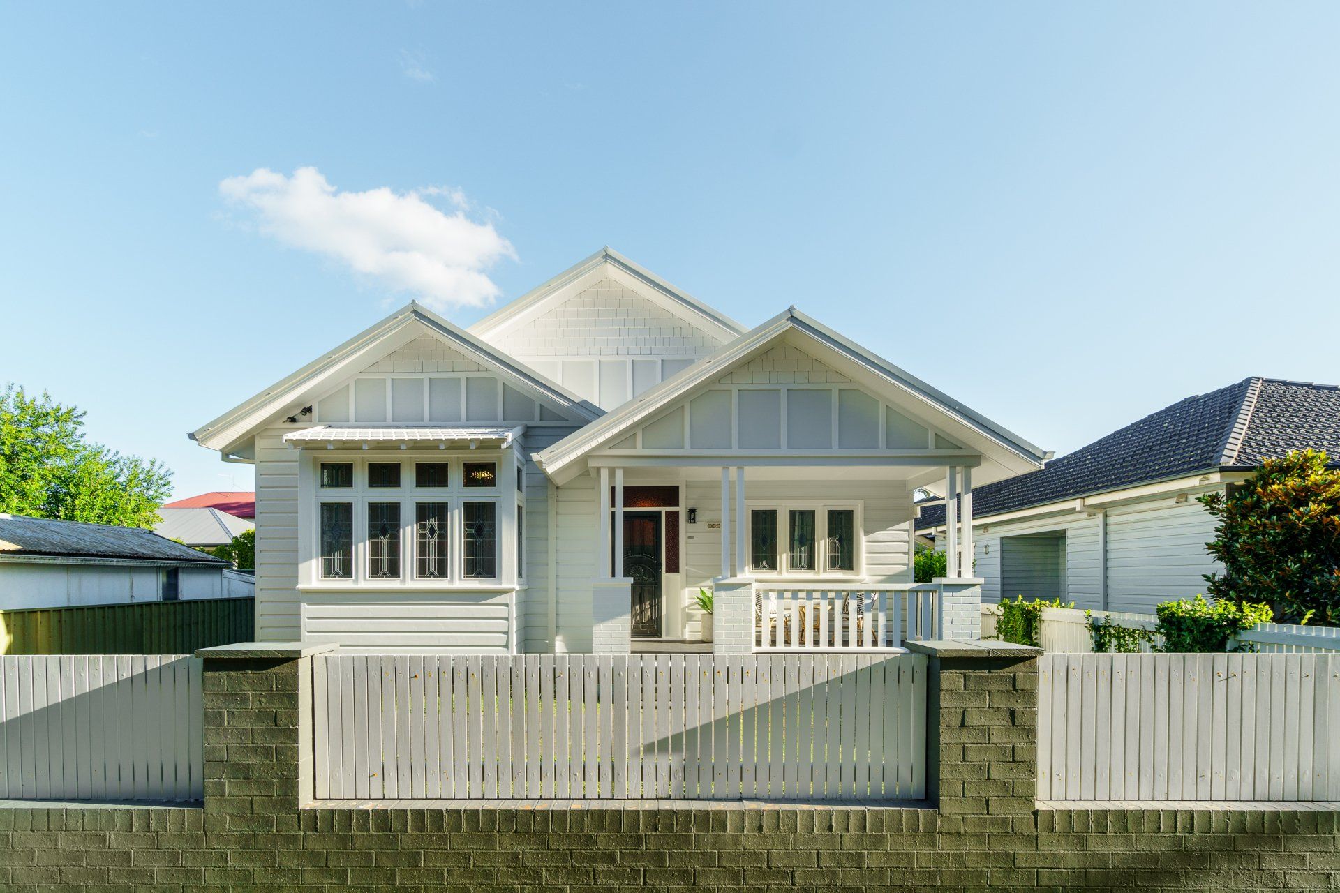 Light grey house with white picket fence and brick accents against a blue sky.