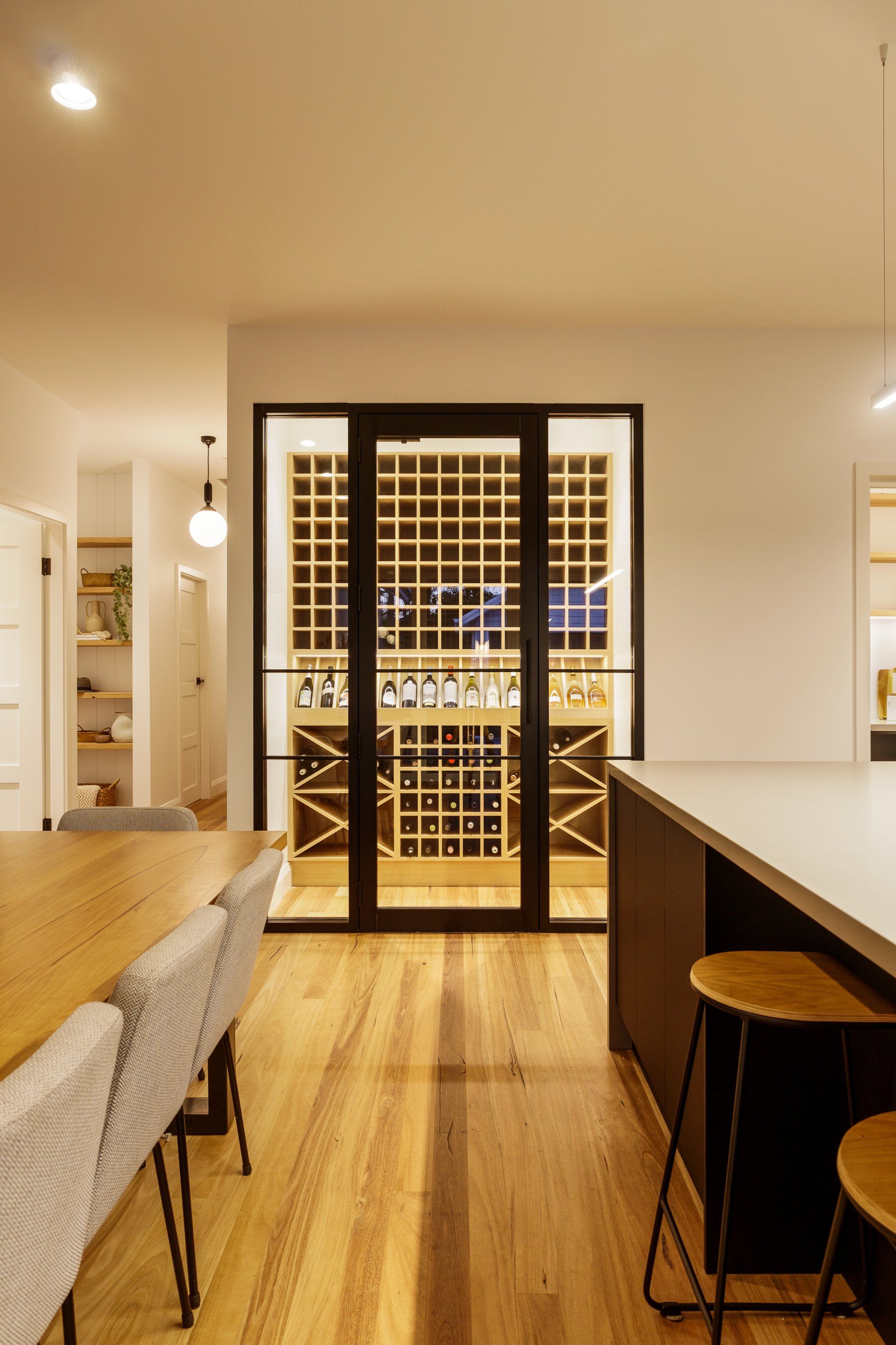 Kitchen interior with wine cellar behind glass doors. Includes a table, chairs, island with stools.