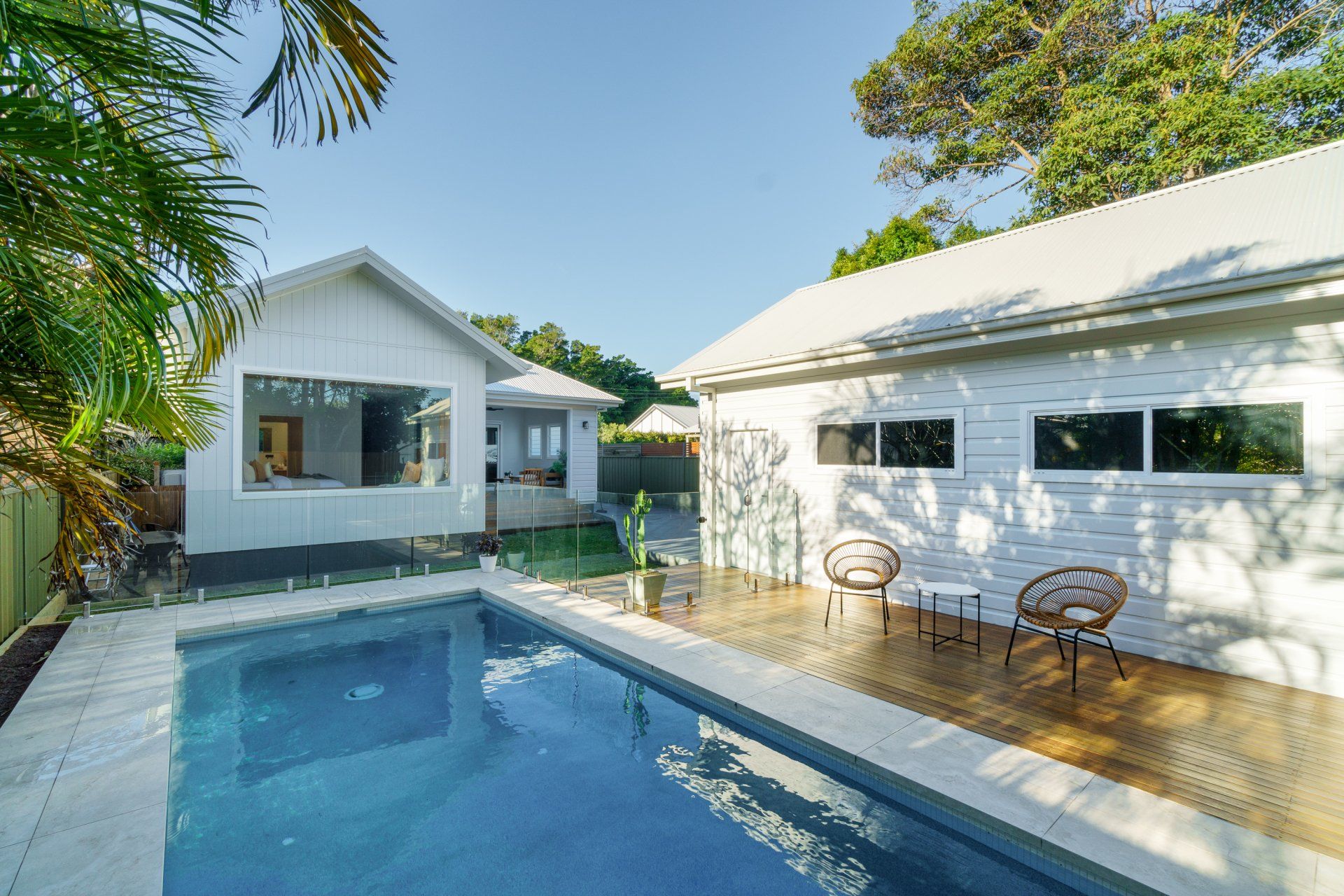 Poolside view of a white house and guest house, with a pool and two chairs.