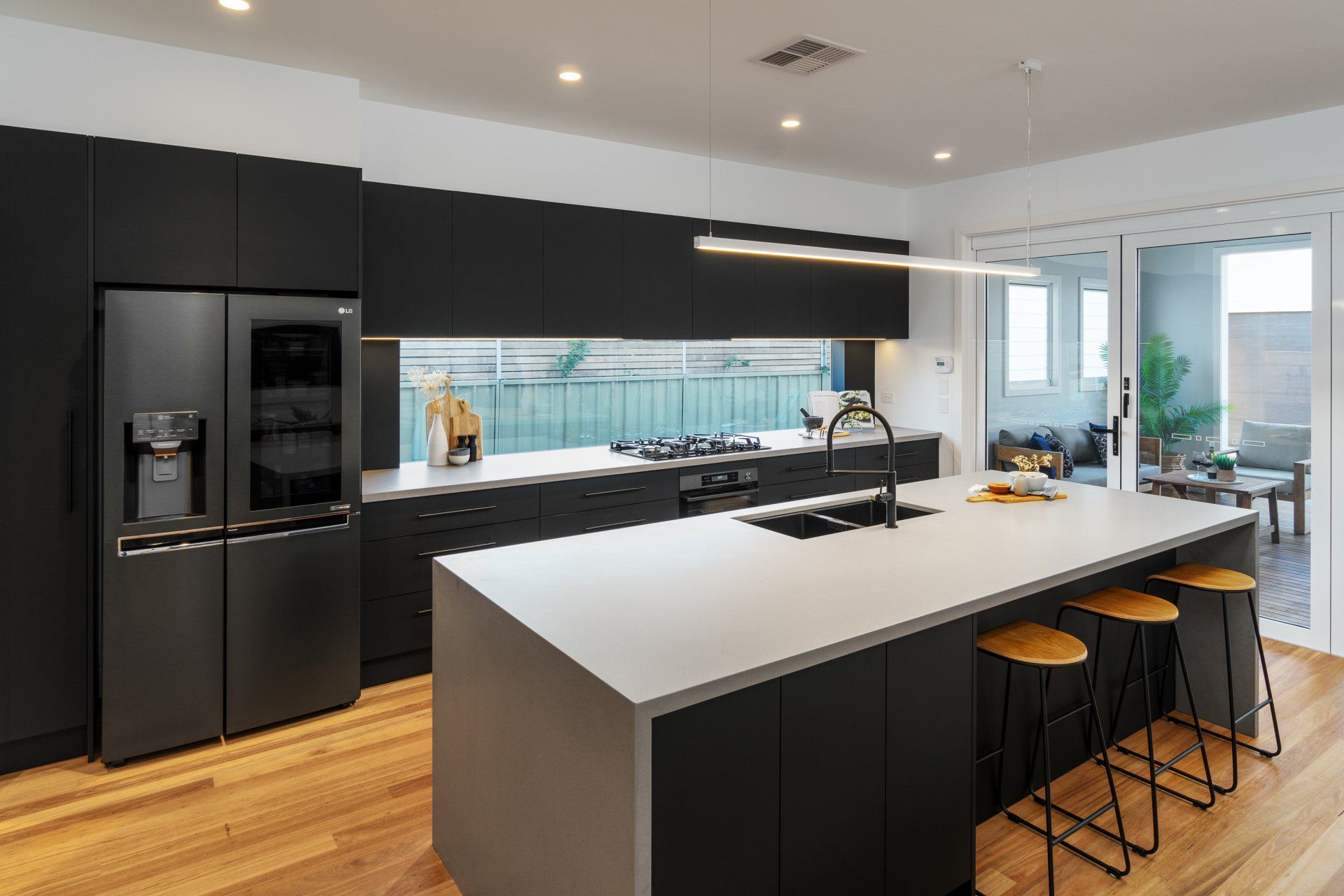 Modern black kitchen with island, stainless steel appliances, and a view to an outdoor patio.