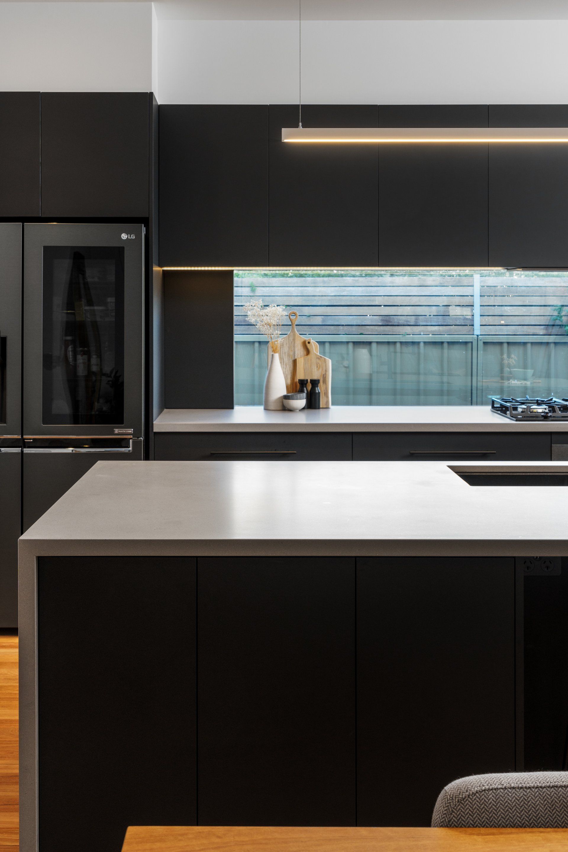 Modern kitchen with black cabinets, gray countertops, and a stainless steel refrigerator.