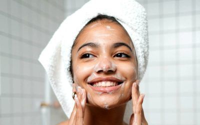 A woman with a towel wrapped around her head is washing her face.
