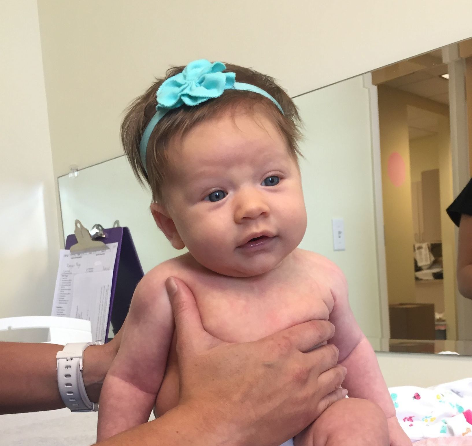 Baby with blue headband being held and examined by a pediatrician