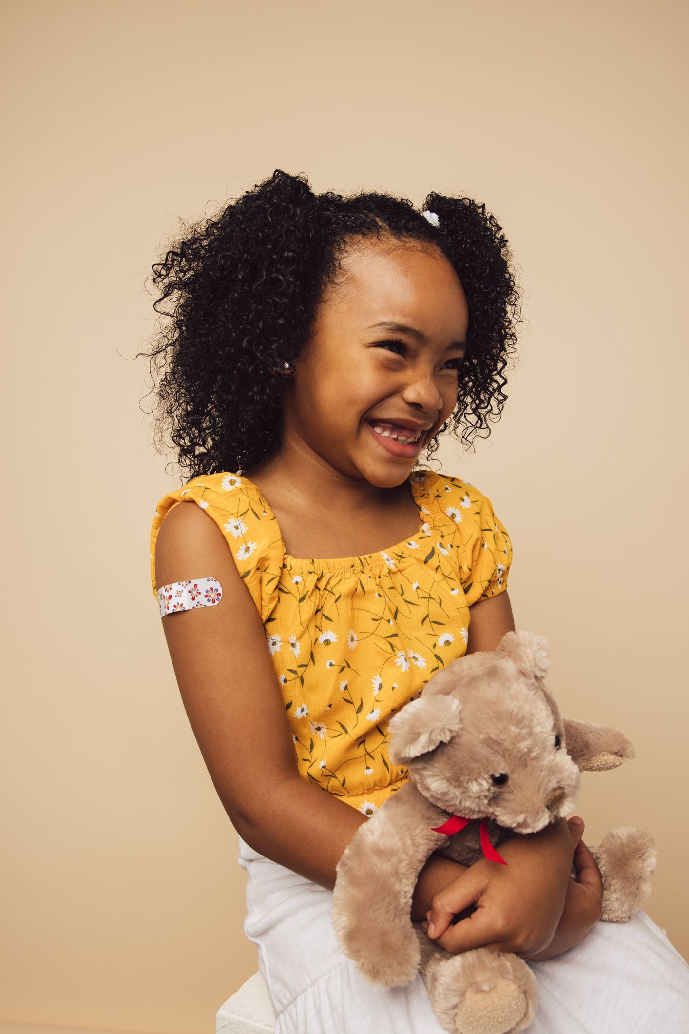 A little girl with a bandage on her arm is holding a teddy bear.