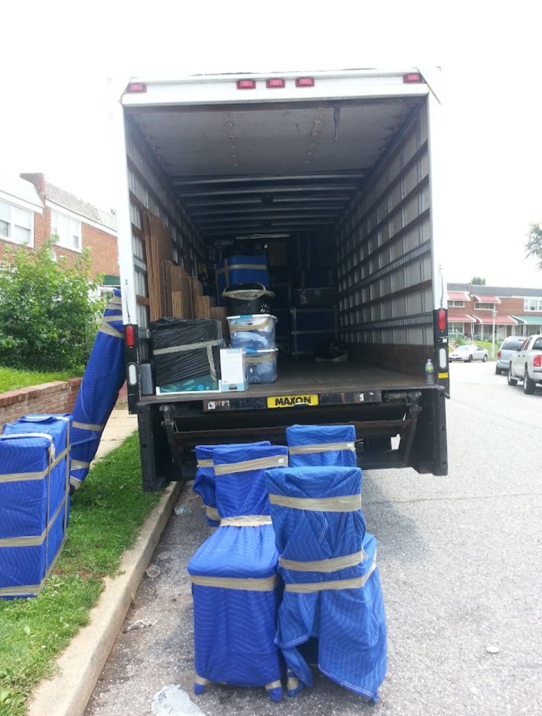 Open truck with blue-wrapped packages being unloaded on a street