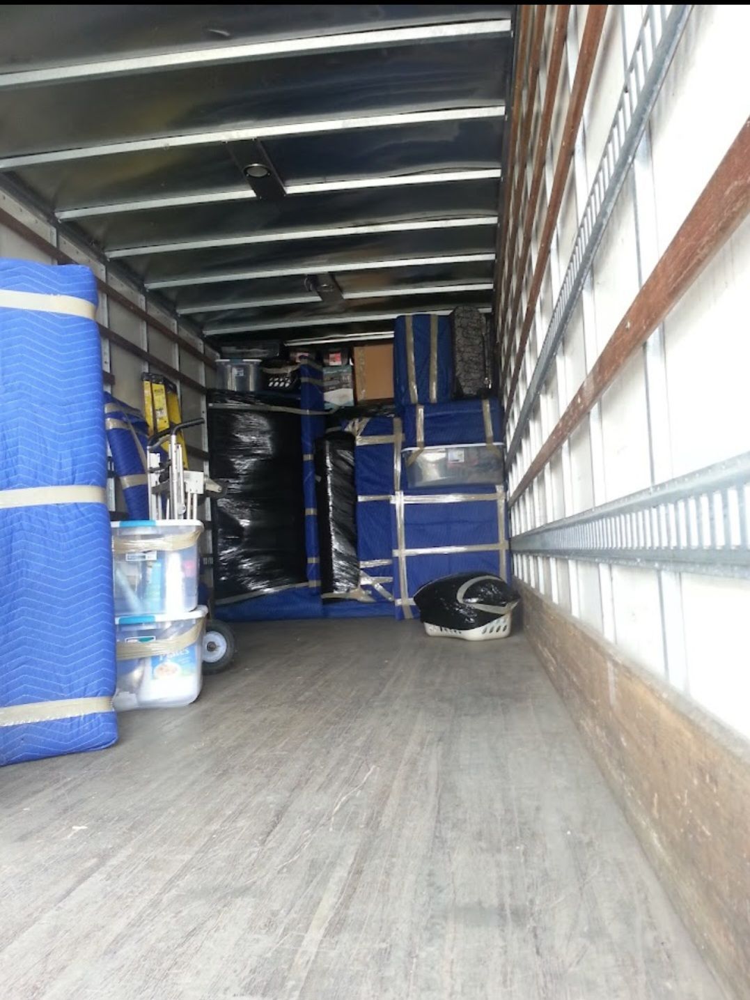Empty moving truck interior with stacked blue-wrapped boxes and equipment along the walls